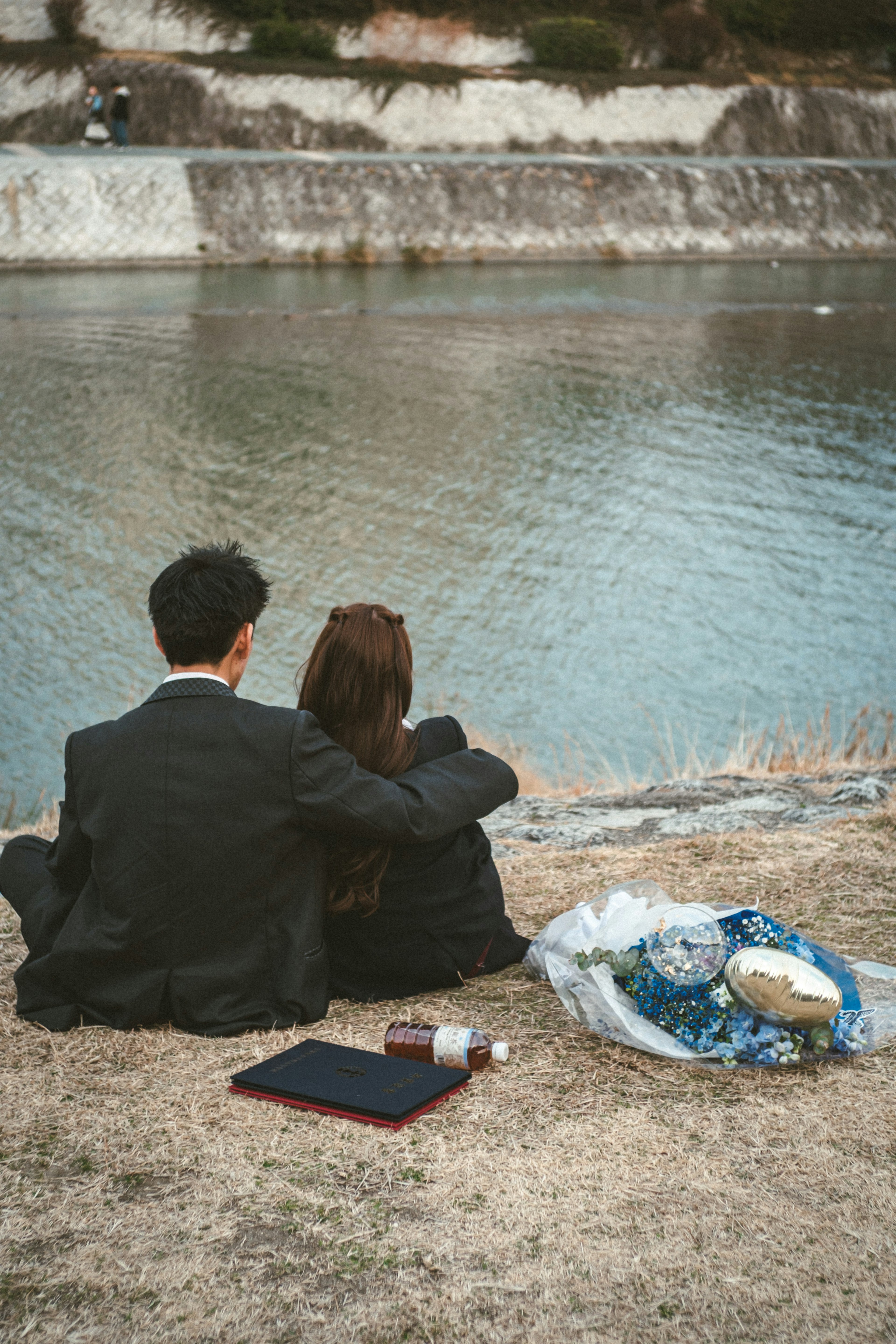 Pareja sentada junto al agua abrazándose en un entorno natural relajado