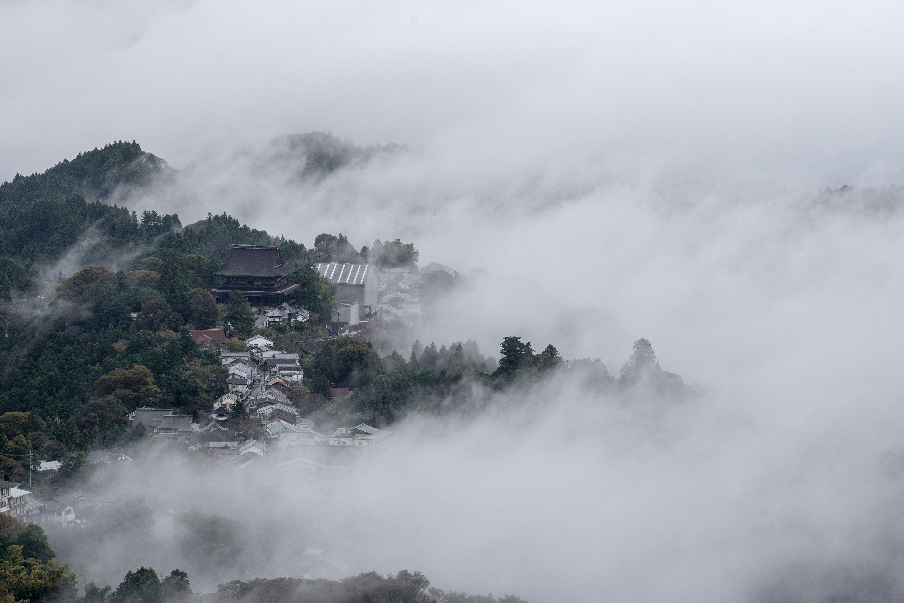 Eine ruhige Dorflandschaft, die in Nebel gehüllt ist, mit Bergen im Hintergrund