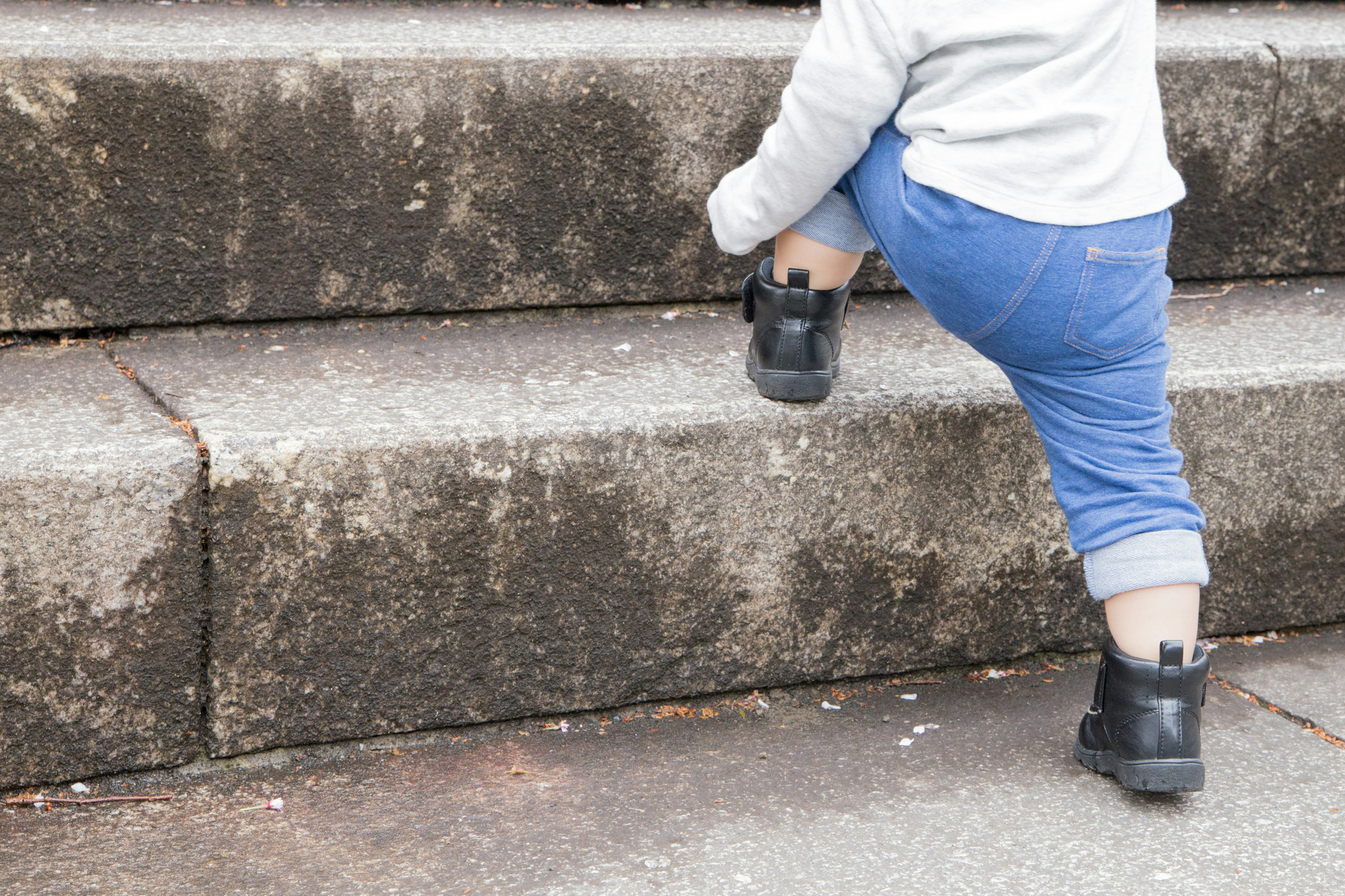 Enfant grimpant des escaliers portant un pantalon bleu et des bottes noires