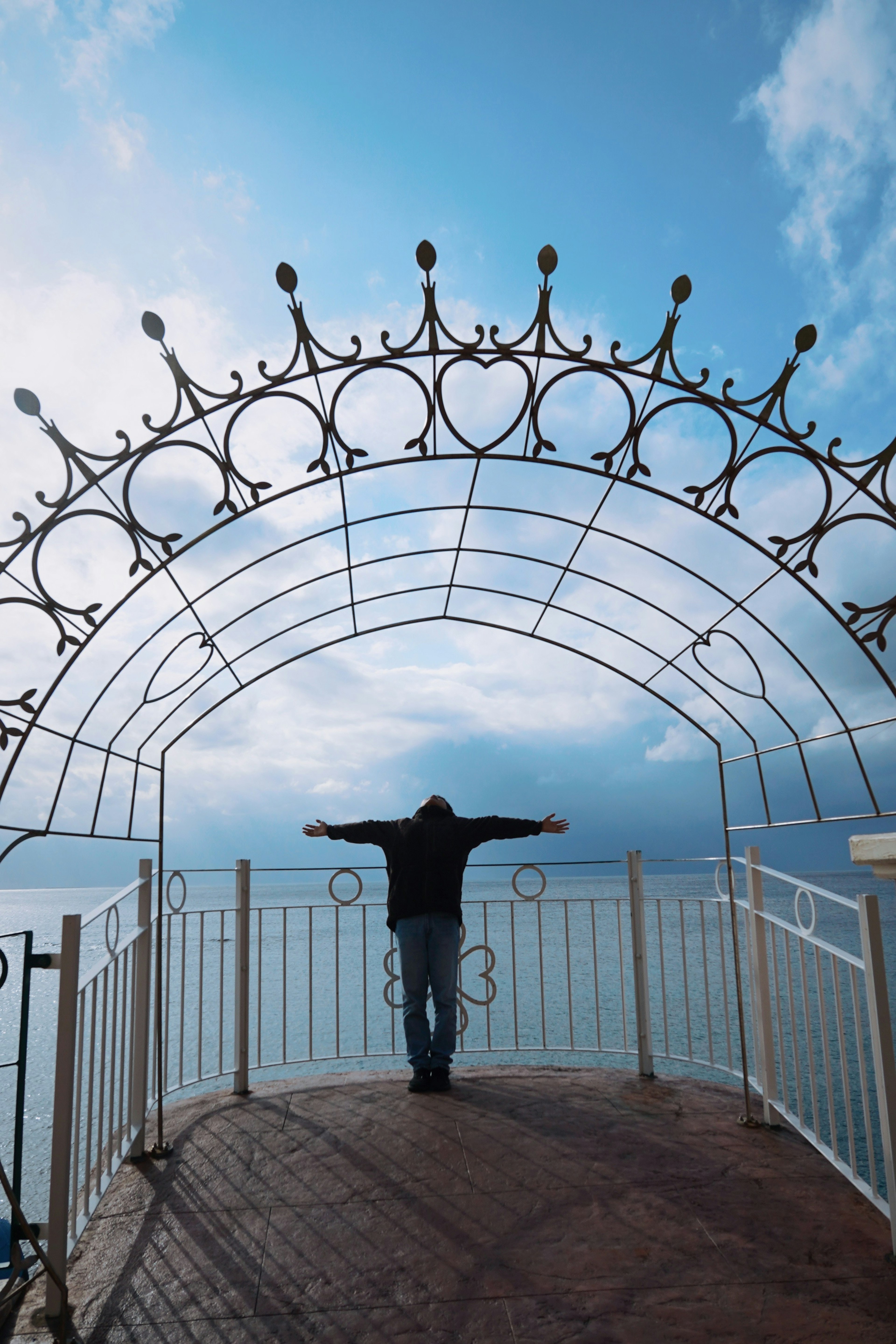 Person with arms outstretched overlooking the sea under a decorative arch