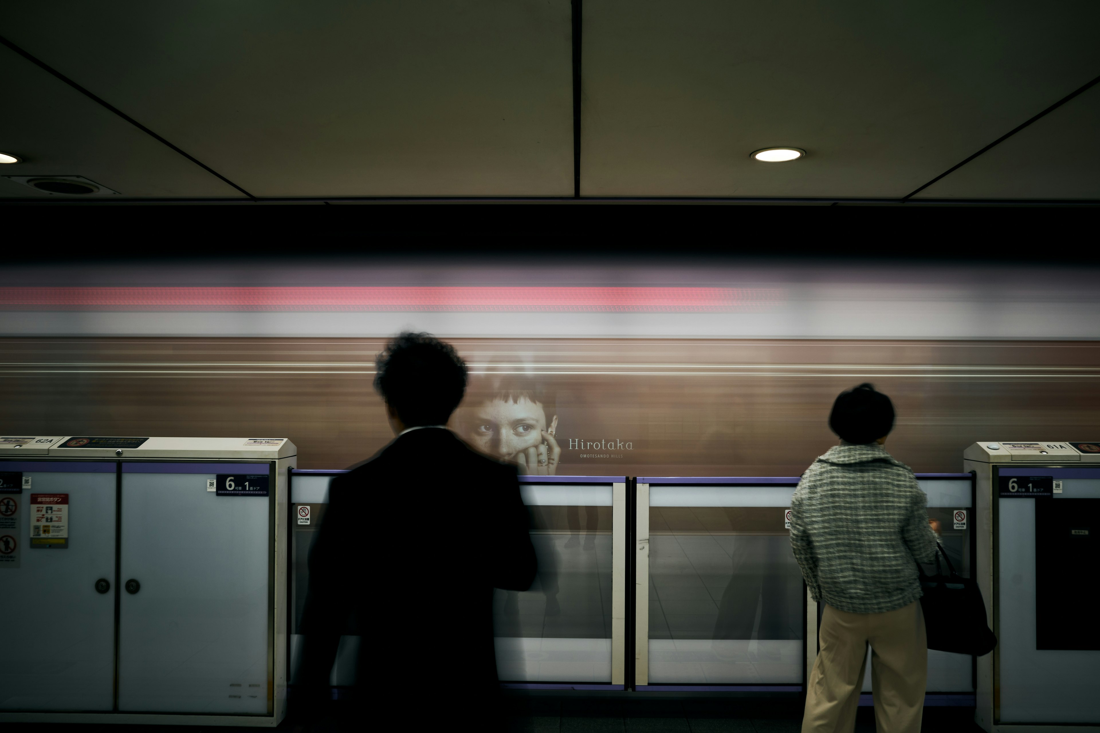 People standing at a train station platform with a blurred train in motion behind them