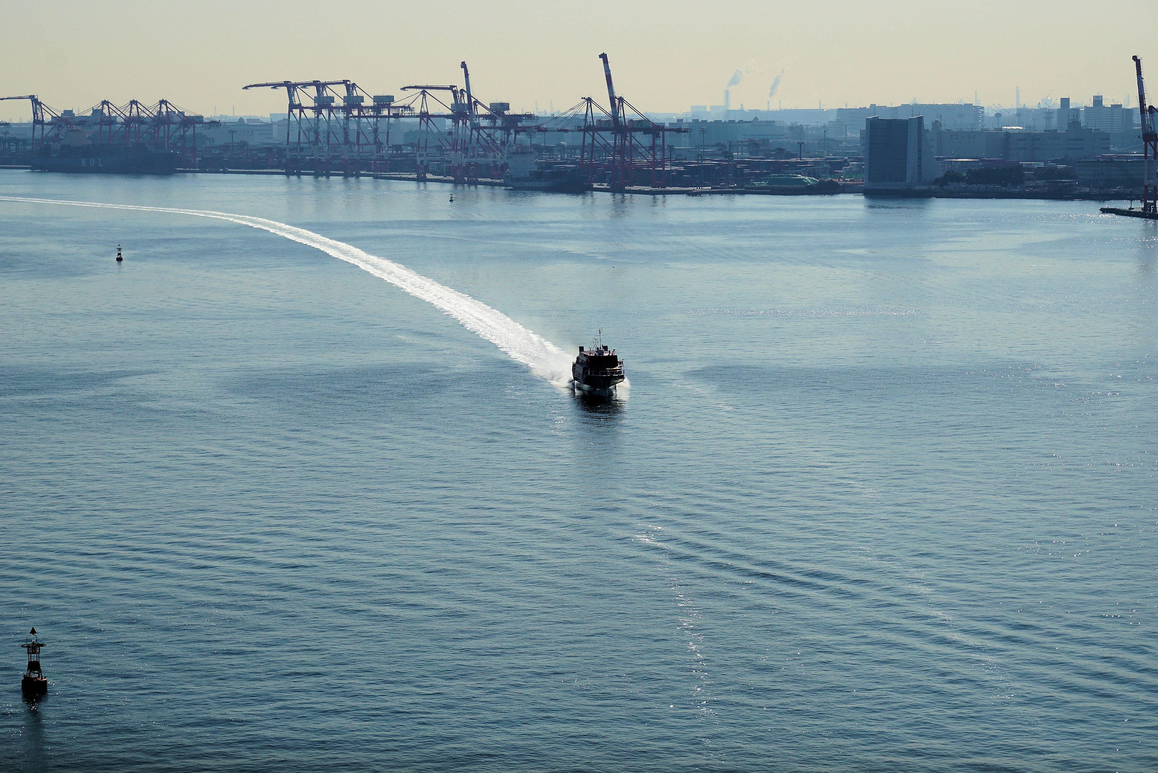 Ein Boot gleitet über ruhiges Wasser mit Hafenkränen im Hintergrund