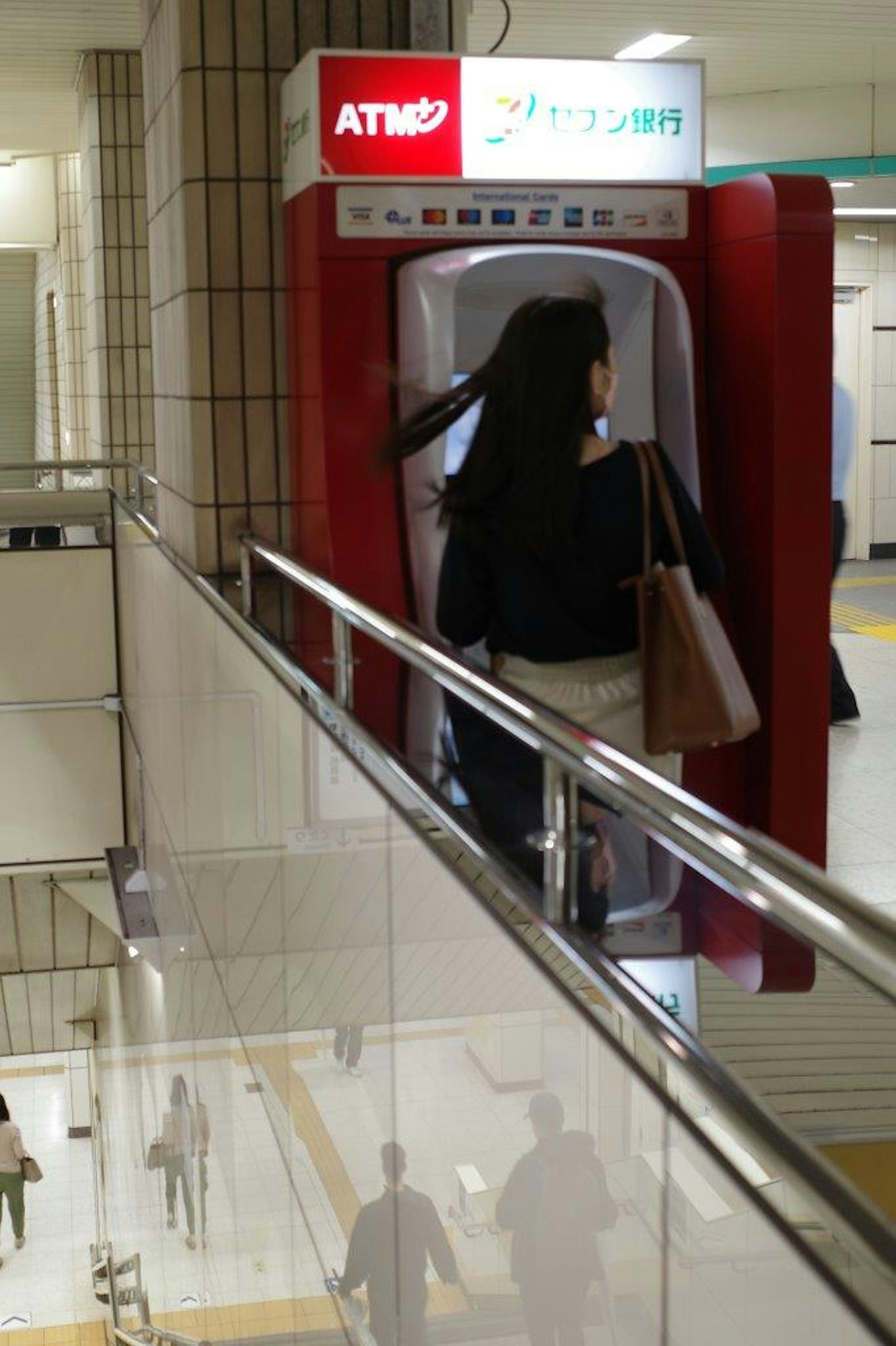 Mesin ATM merah dengan seorang wanita di dekatnya di lingkungan stasiun