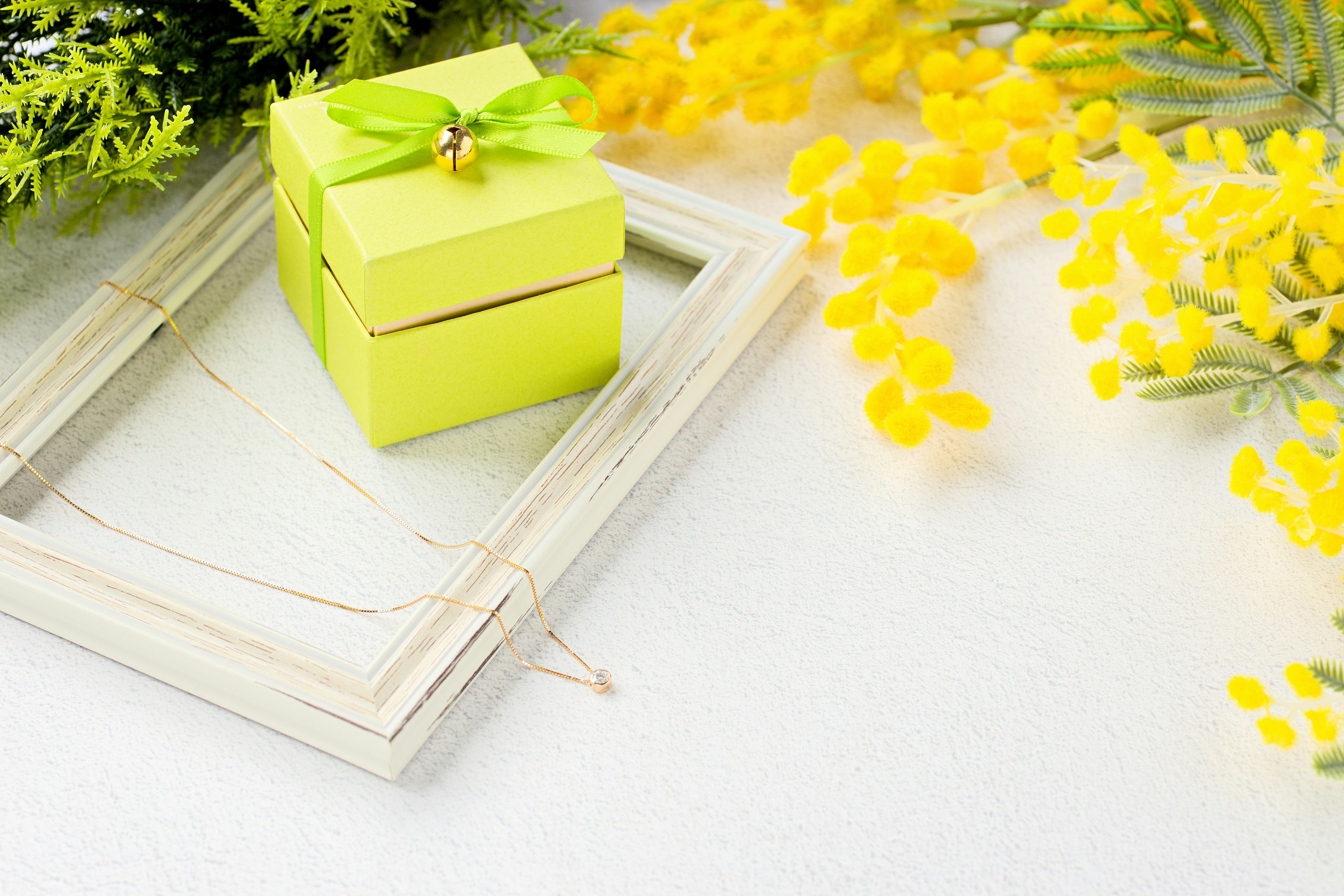 Kleine gelbe Geschenkbox mit grünem Band umgeben von gelben Blumen und einem Rahmen