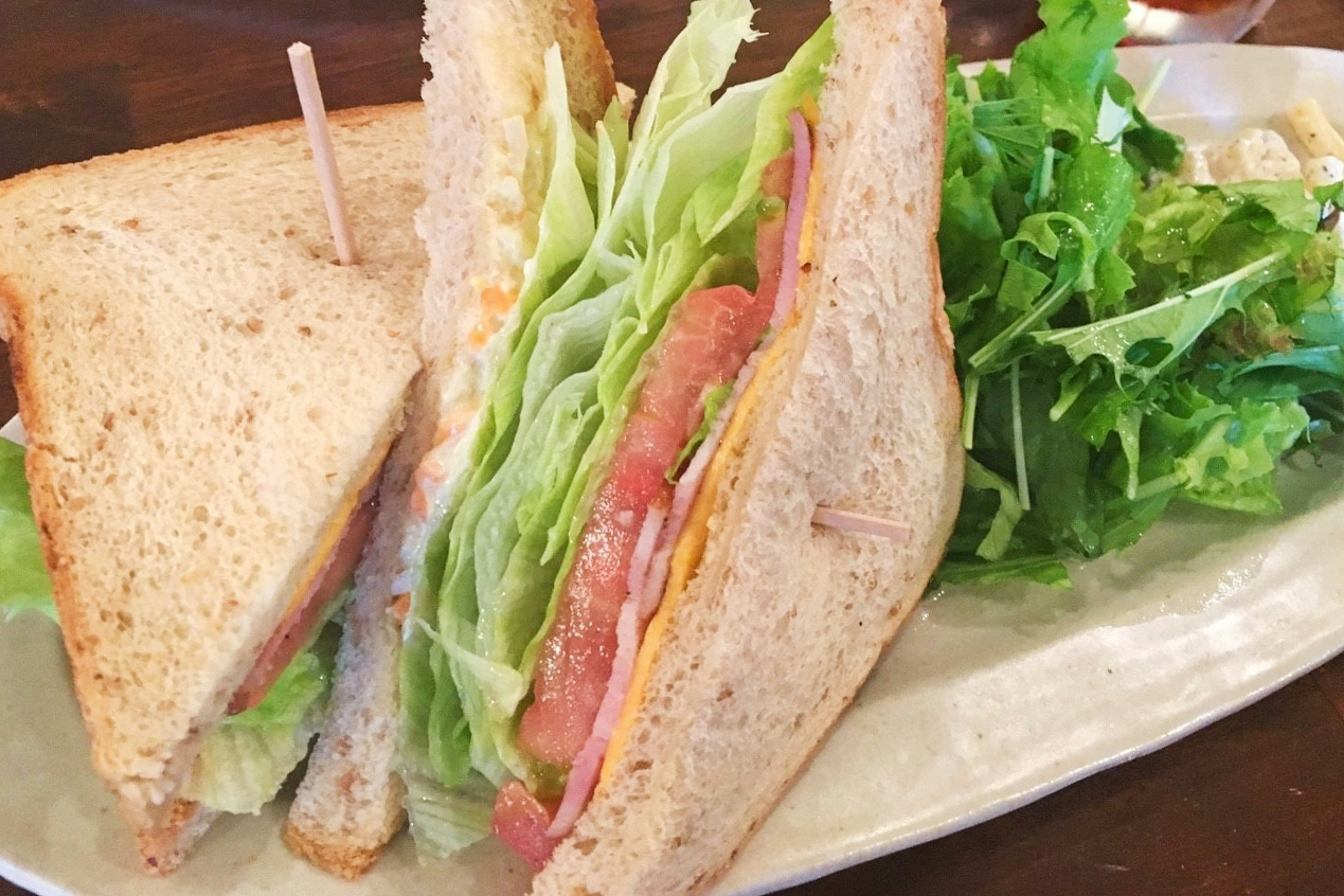 Một đĩa có bánh sandwich với bánh mì nguyên cám chứa xà lách giăm bông và phô mai bên cạnh là một đĩa salad xanh