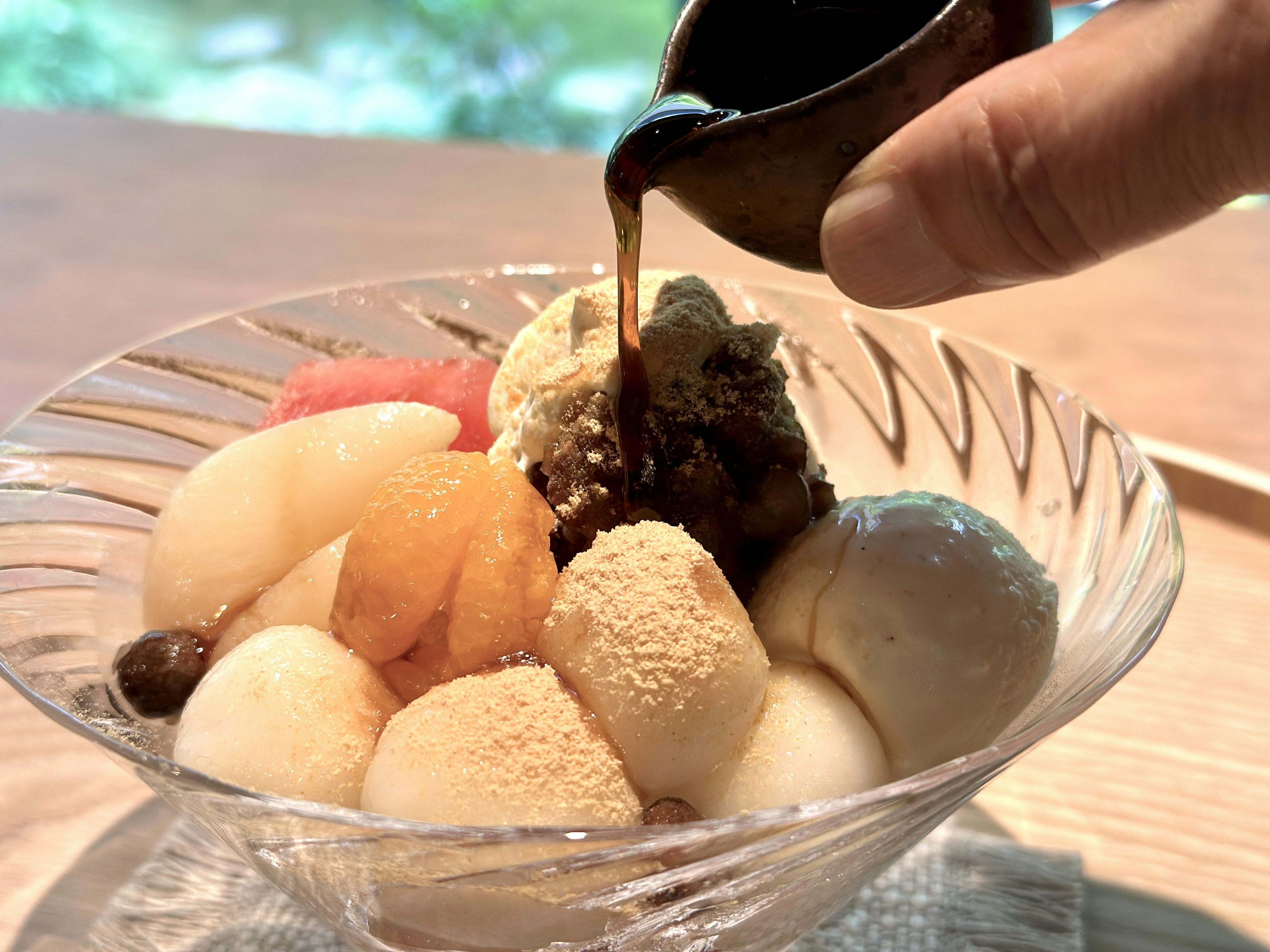 A hand pouring sweet sauce over a colorful dessert bowl