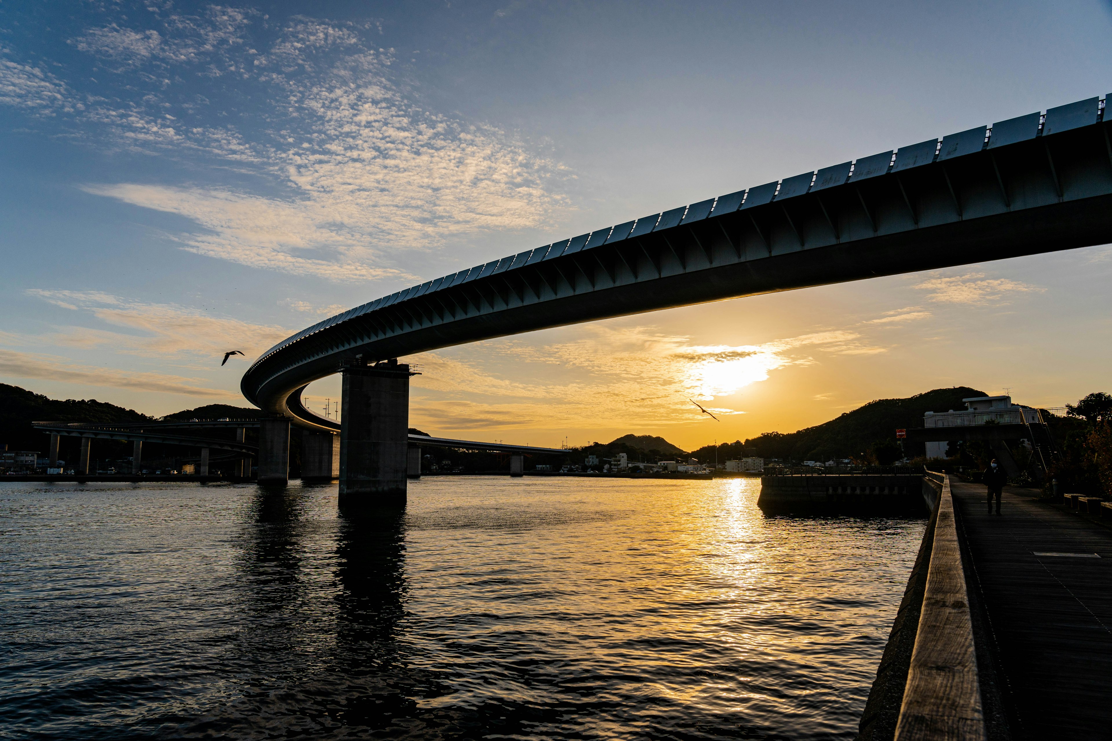 Puente elevado curvado sobre el agua con fondo de atardecer