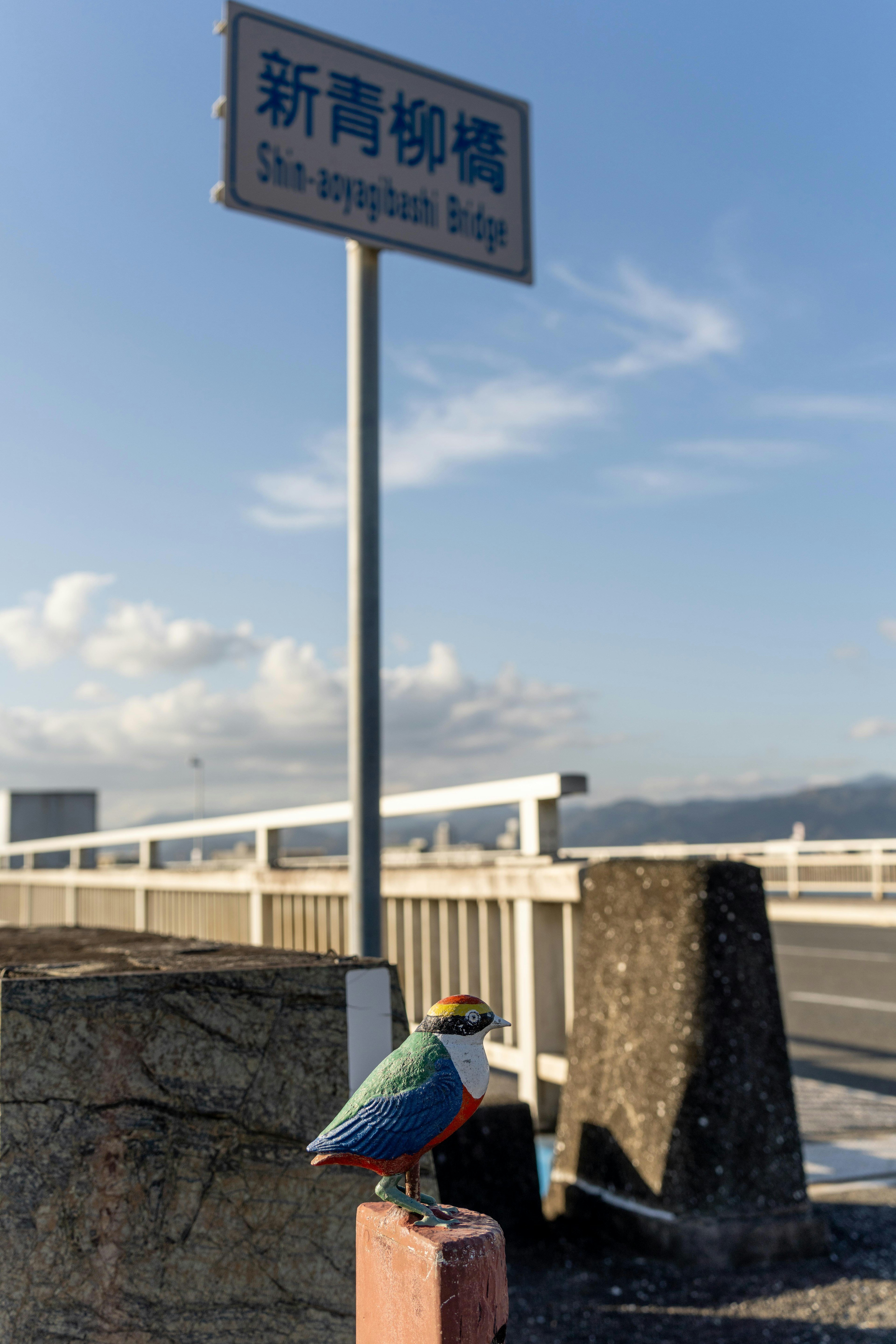 Scene featuring a sign for Shin-Hashi and a colorful bird sculpture