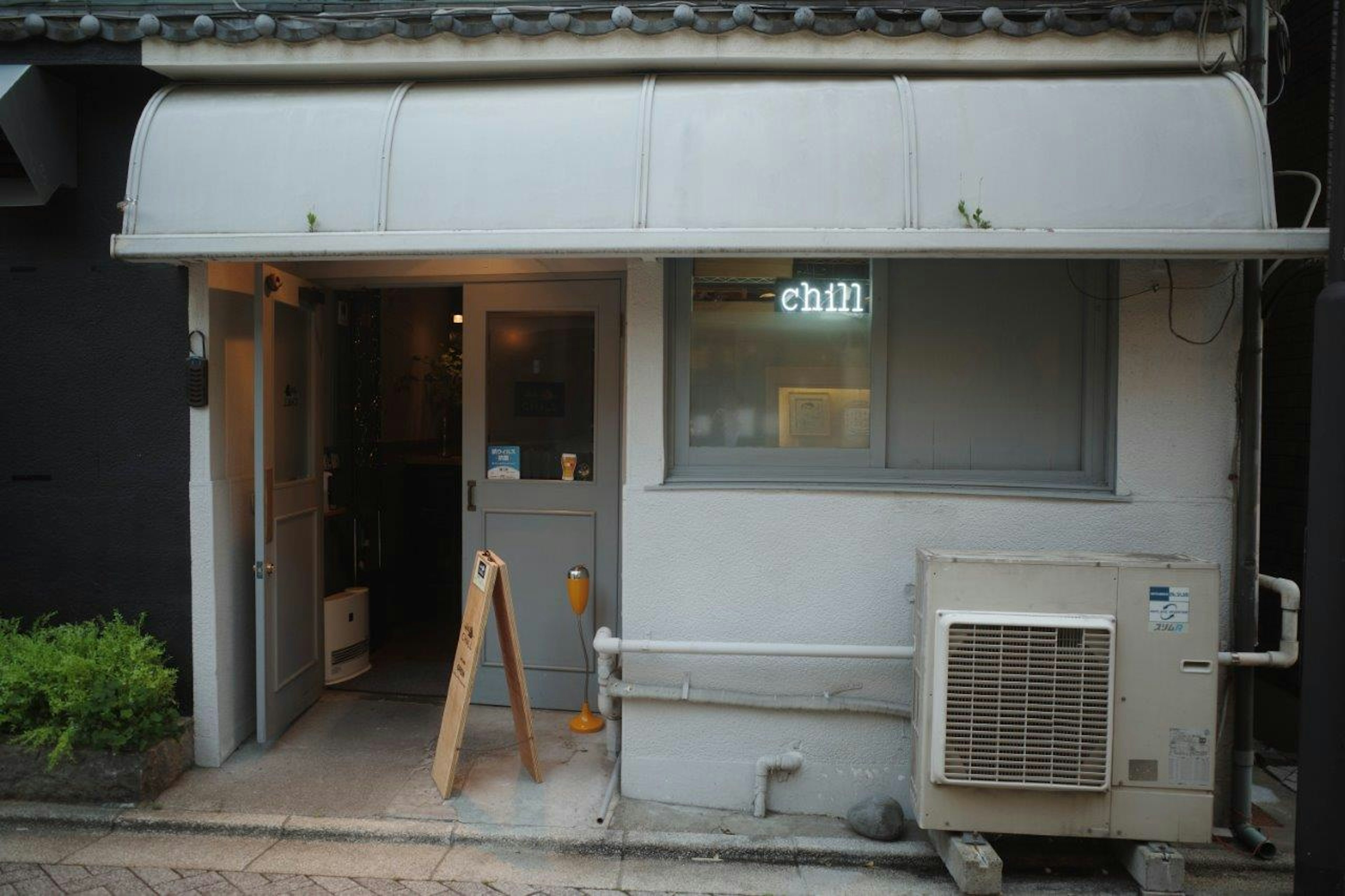 シンプルな外観のカフェの入り口 壁に取り付けられたエアコン 木製の看板が特徴