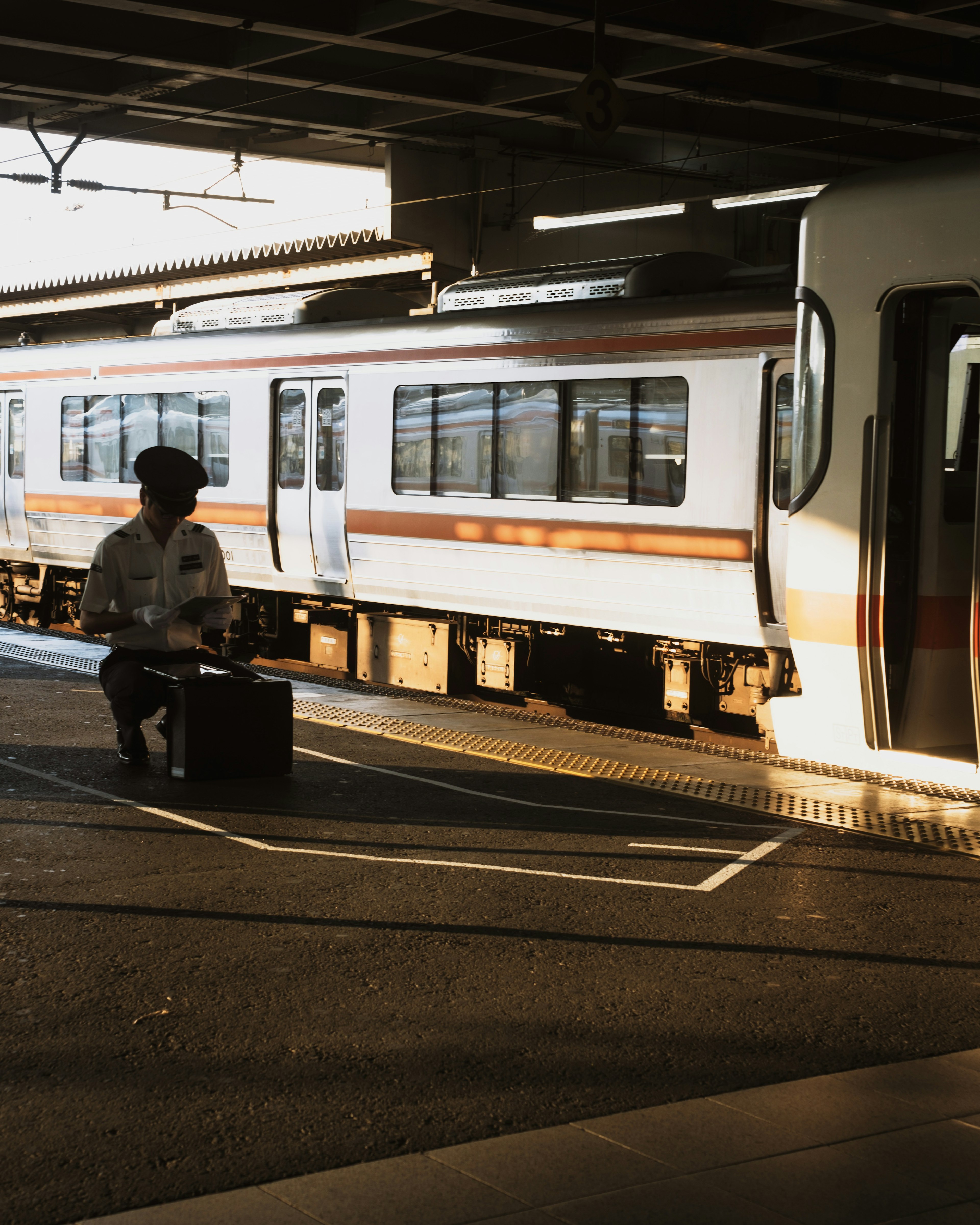 A man sitting on a suitcase at a train station platform with a train in the background