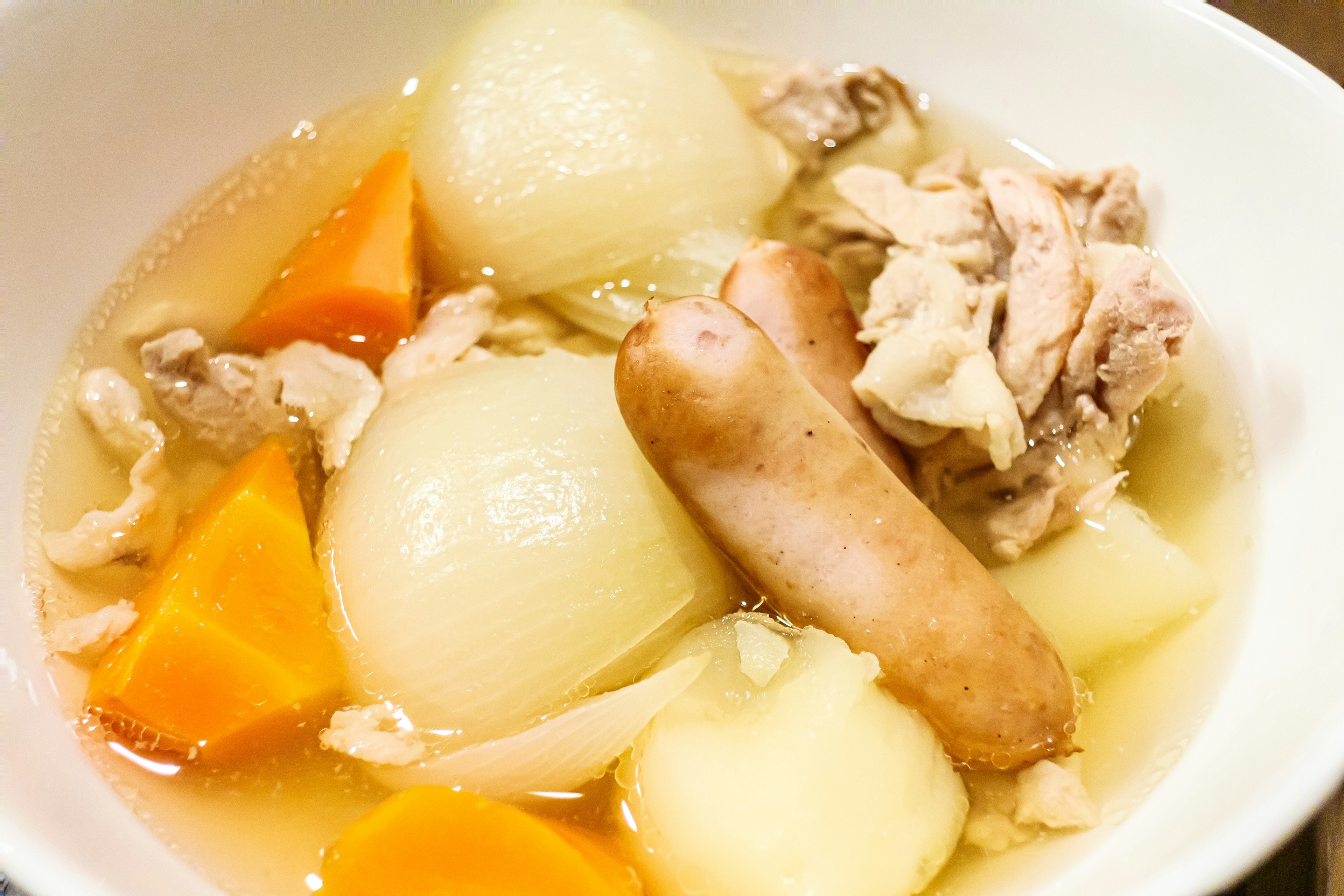 A bowl of chicken and vegetable soup with carrots potatoes and sausage