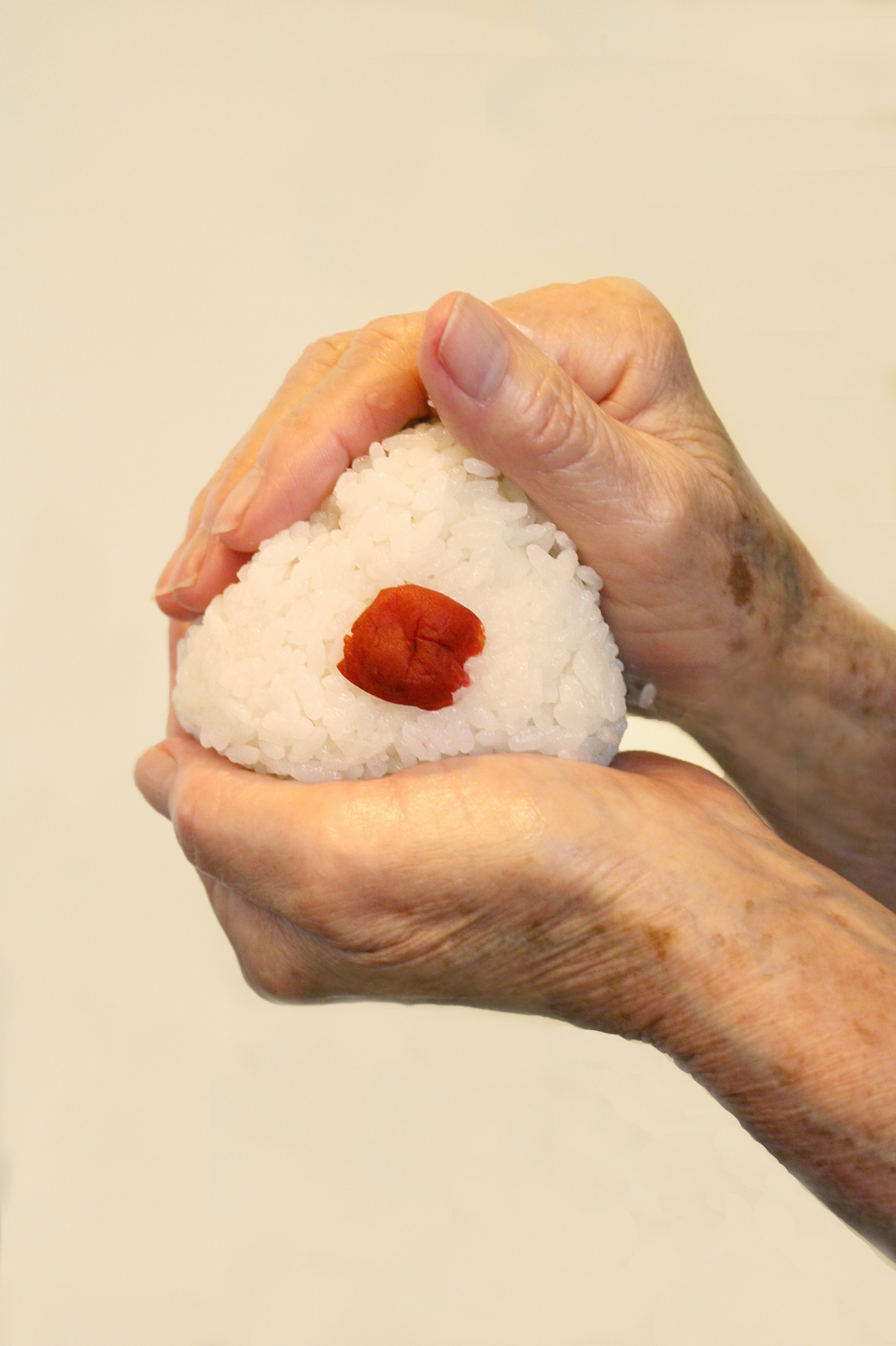 Hände formen einen Reisbällchen mit einer roten Pflaume in der Mitte