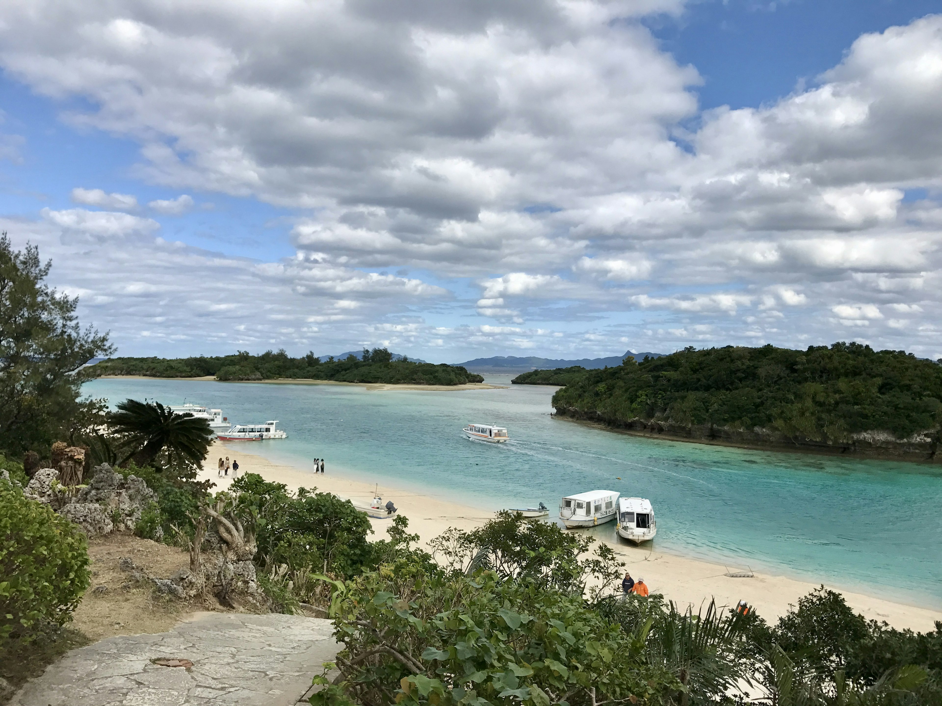 ทิวทัศน์ที่สวยงามของชายหาดที่มีน้ำสีเขียวมรกตและเรือใกล้เกาะเขียวขจี