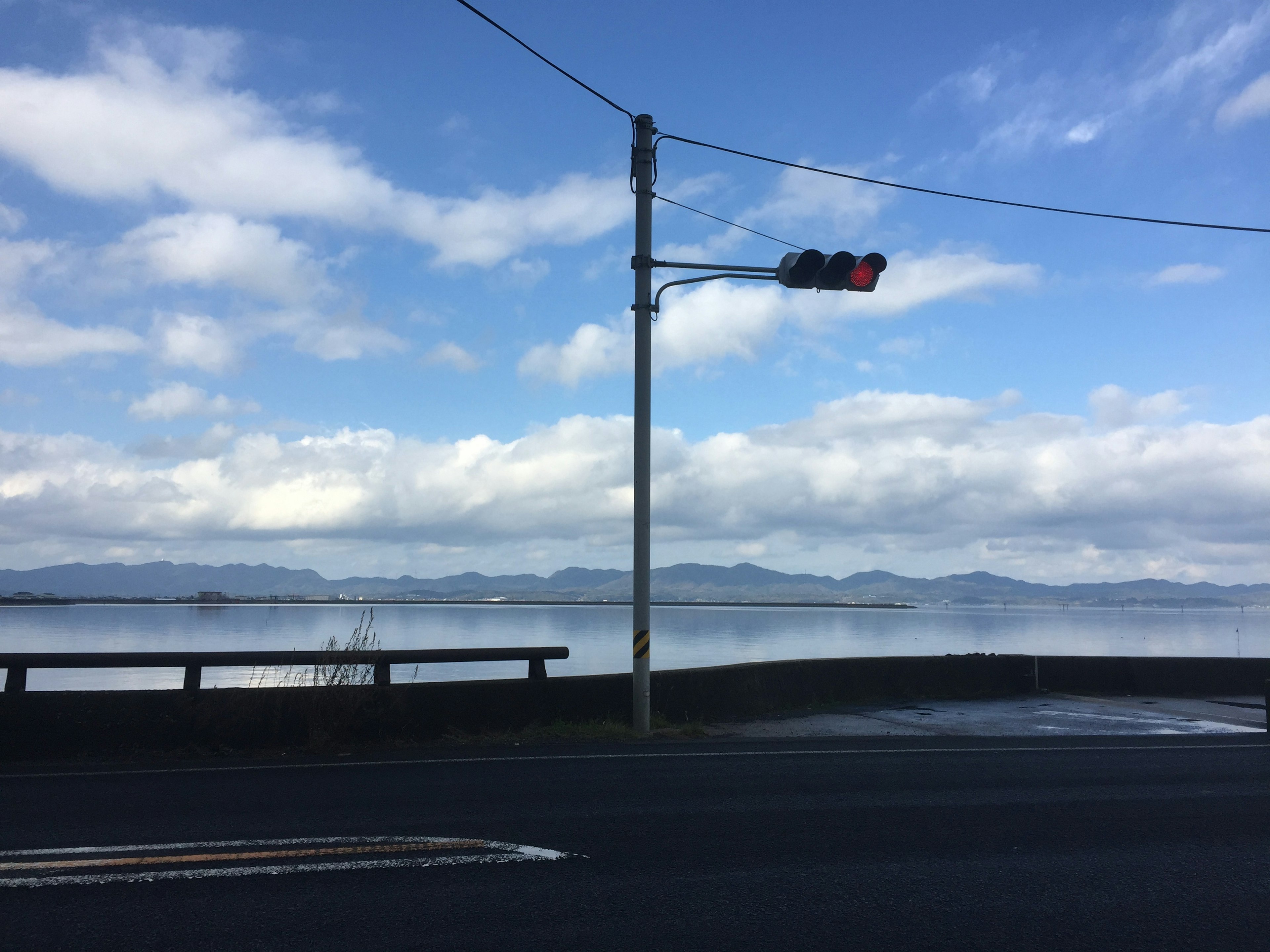 Semáforo junto a un lago sereno bajo un cielo azul con nubes