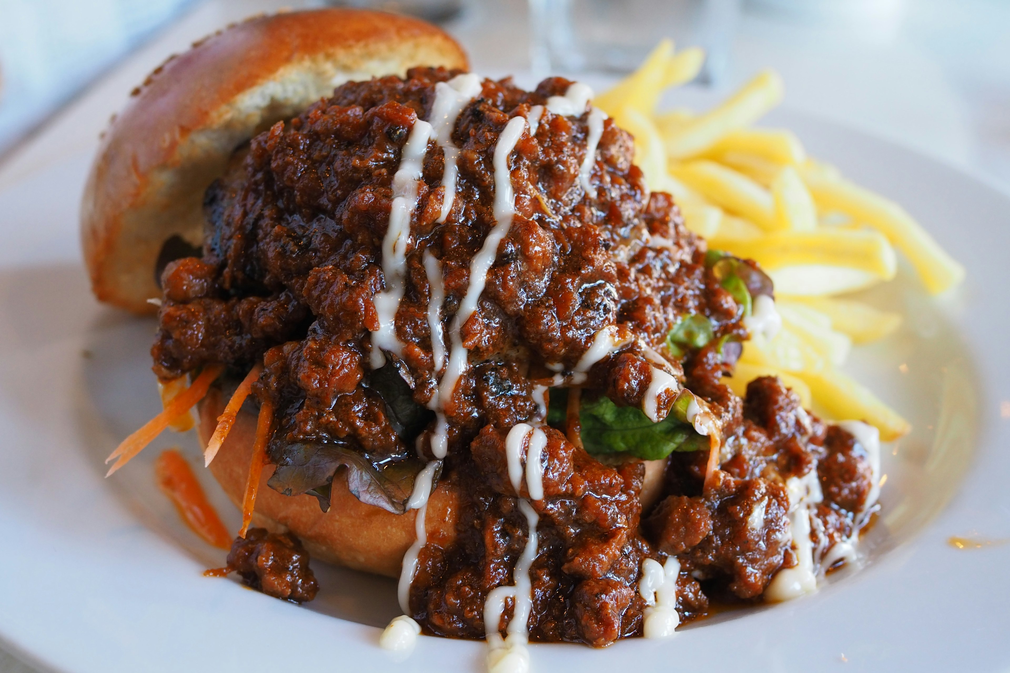 A plate featuring a burger topped with rich meat sauce and served with fries