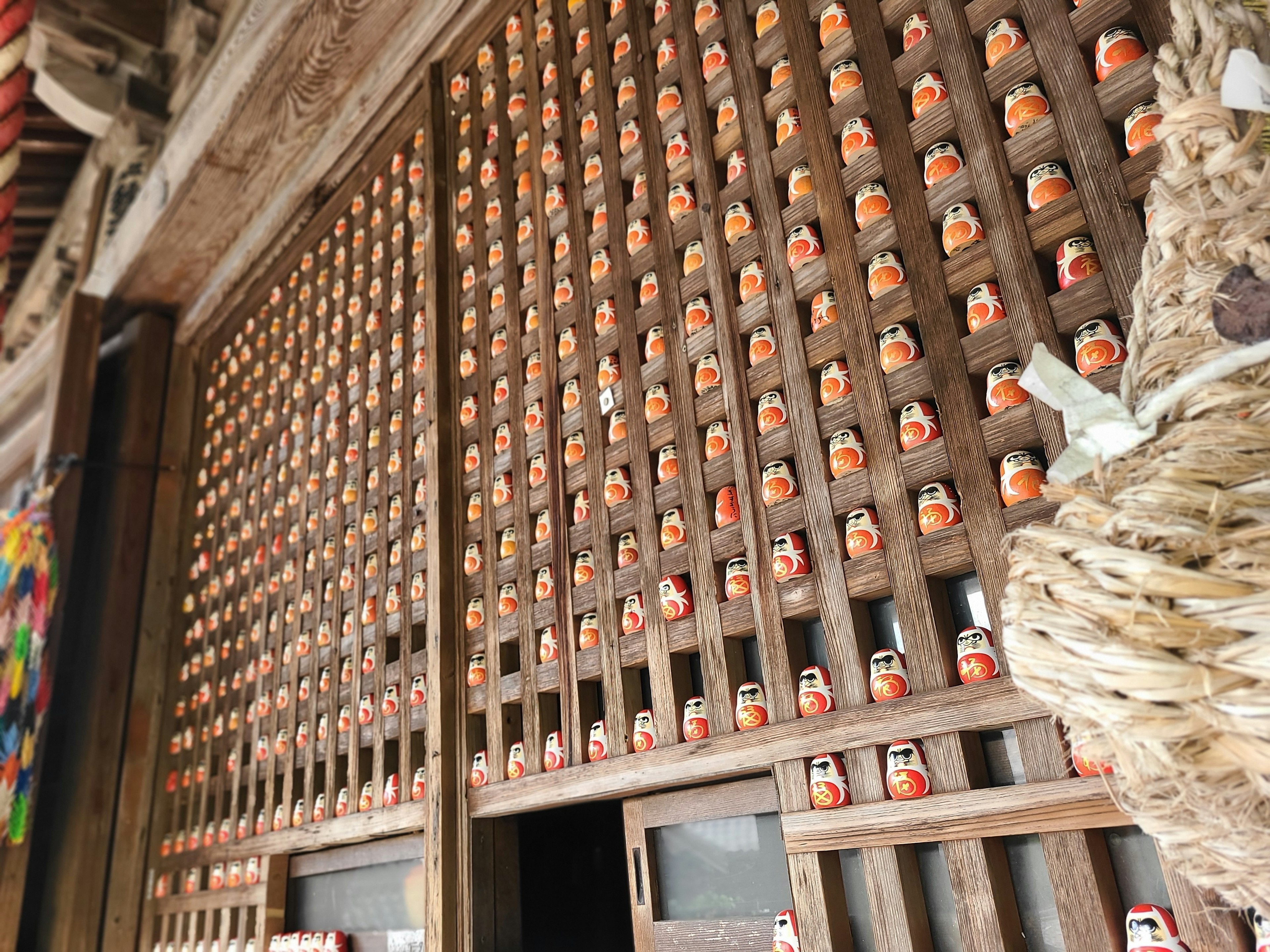 Innenraum eines traditionellen japanischen Gebäudes mit einer Holzwand, die mit kleinen Puppen bedeckt ist