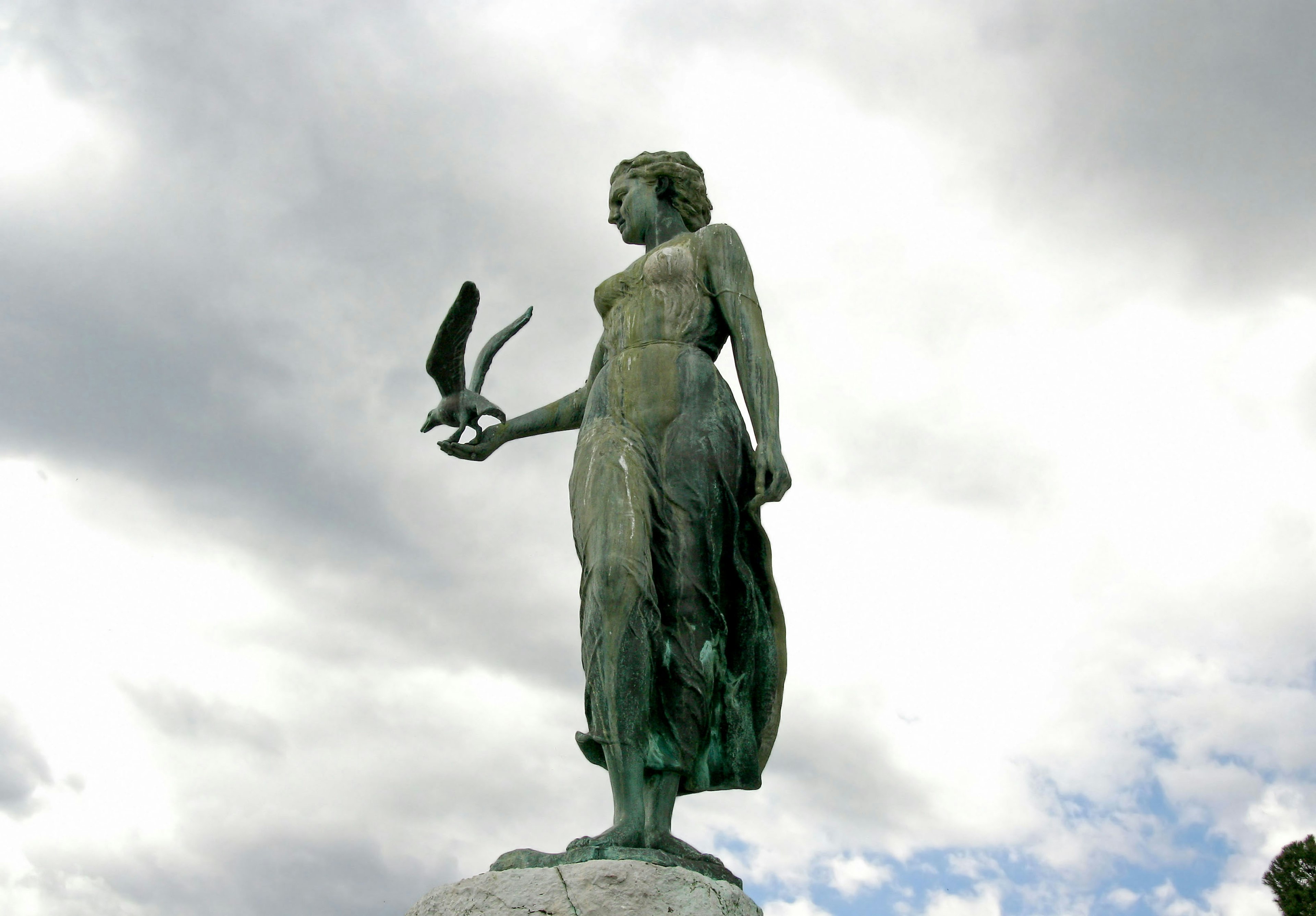 Una estatua femenina sosteniendo un pájaro bajo el cielo