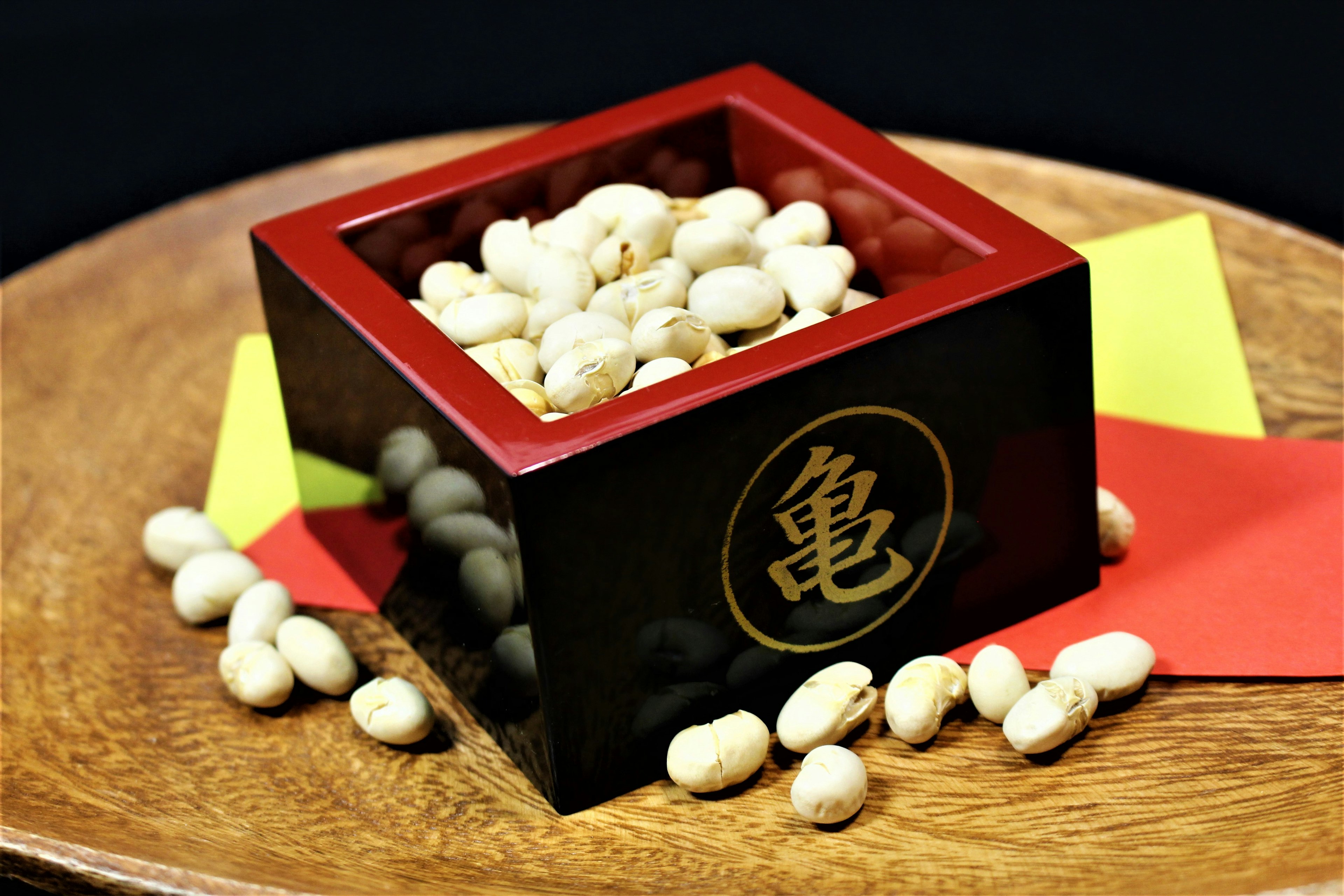 Caja cuadrada con acentos rojos llena de frijoles blancos sobre un plato de madera