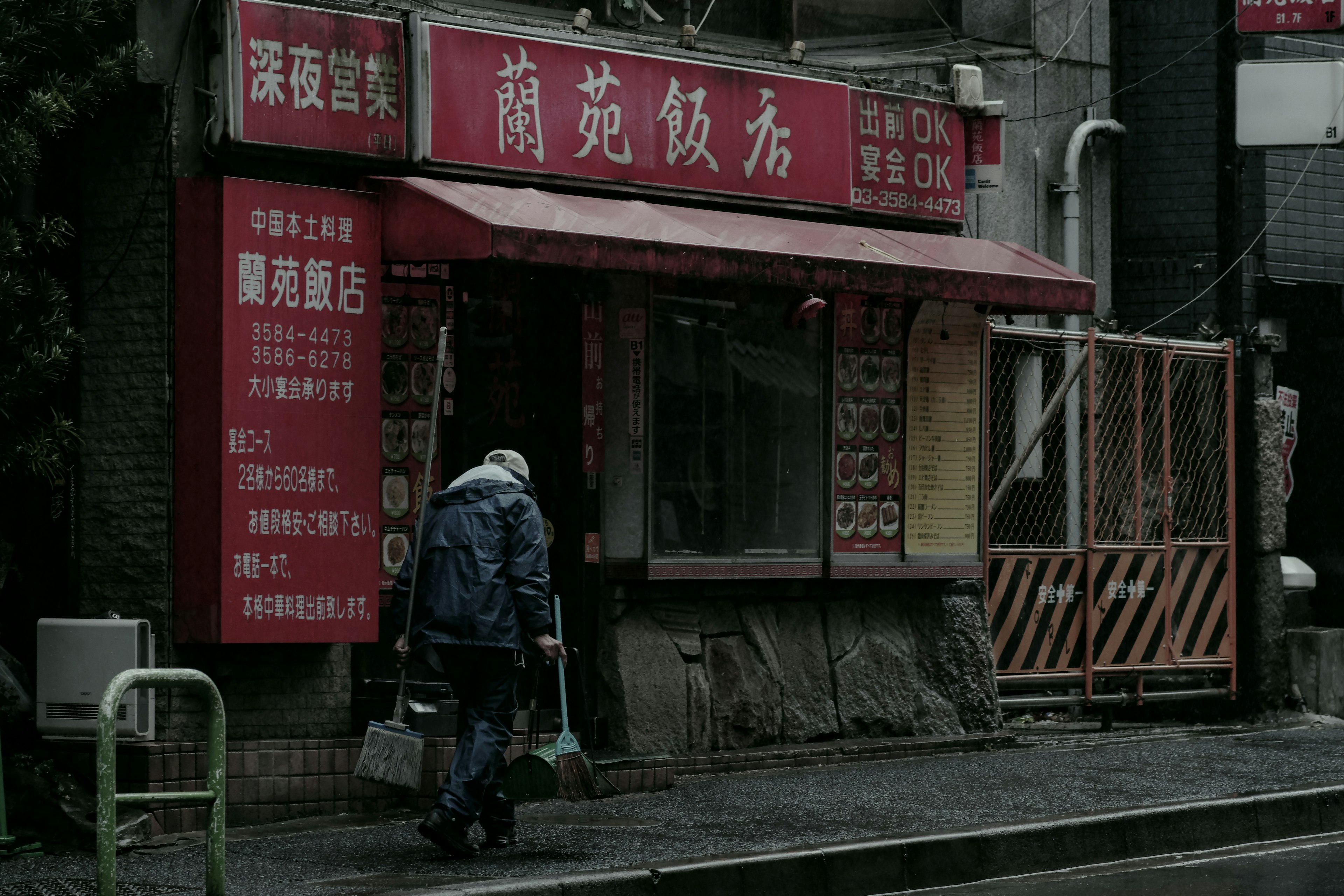 A dimly lit street corner with a red sign restaurant and a person walking