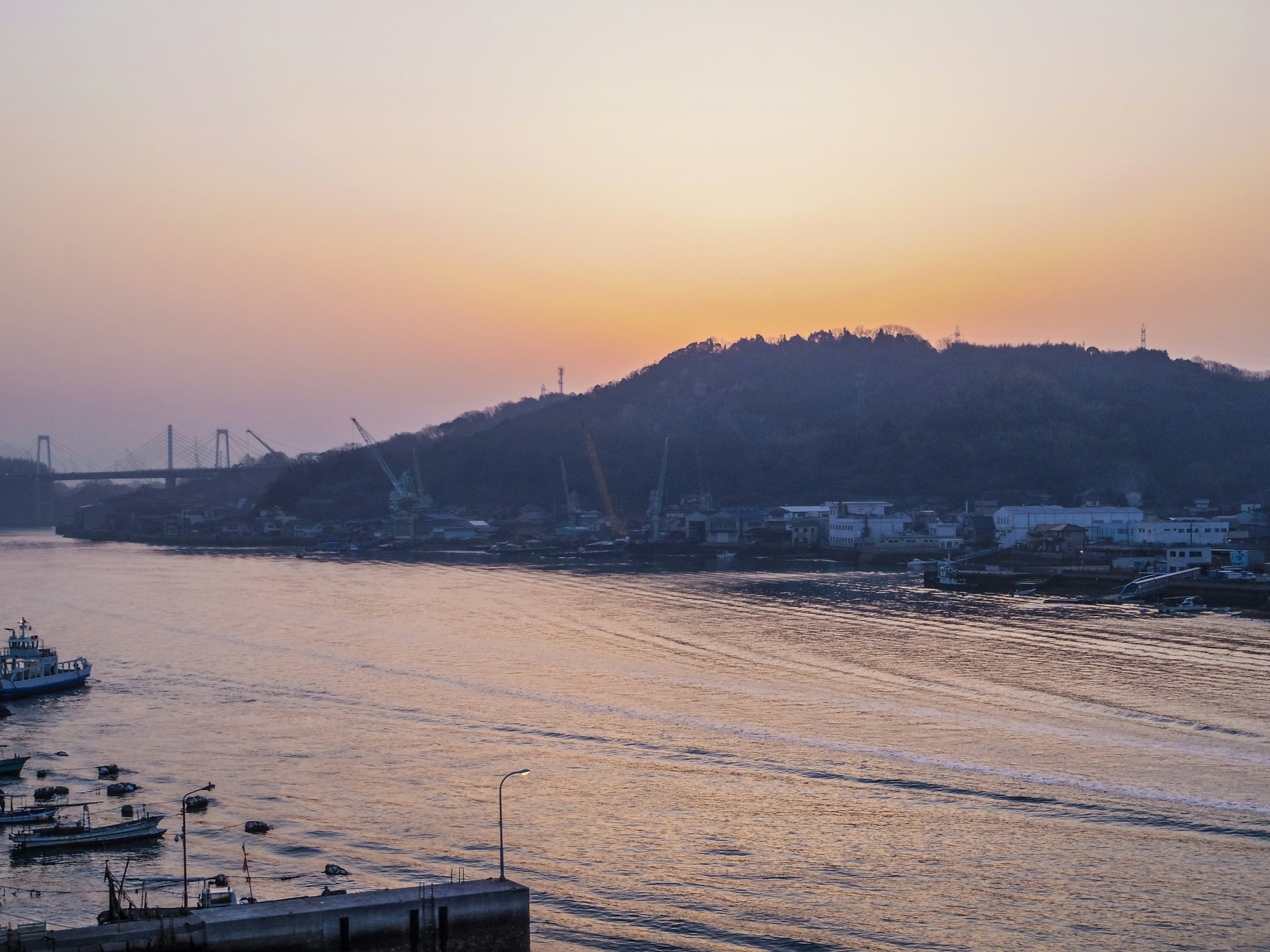 Vista del tramonto su un fiume con barche e una collina sullo sfondo