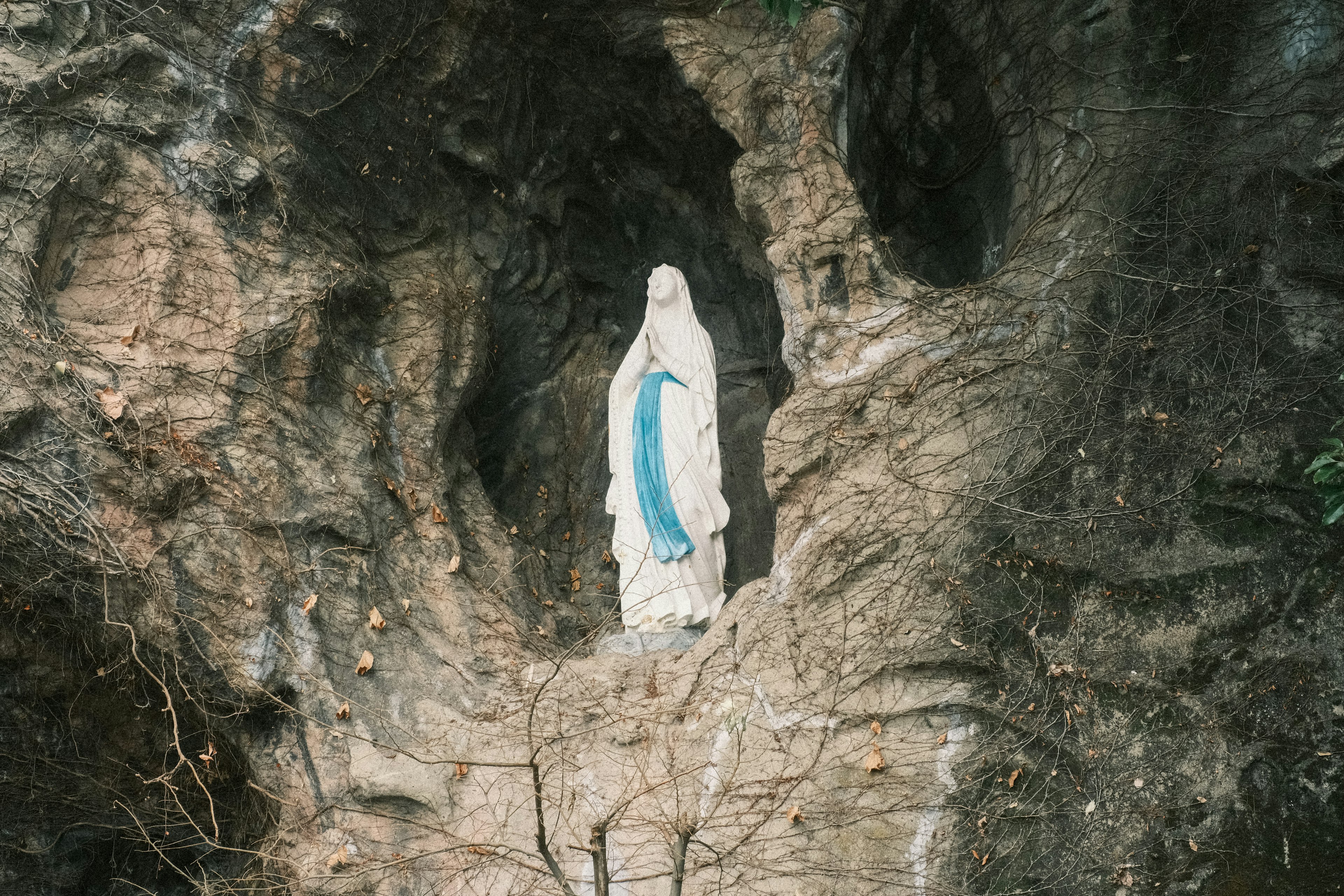 Statue de la Vierge Marie se tenant dans une grotte rocheuse portant un manteau bleu