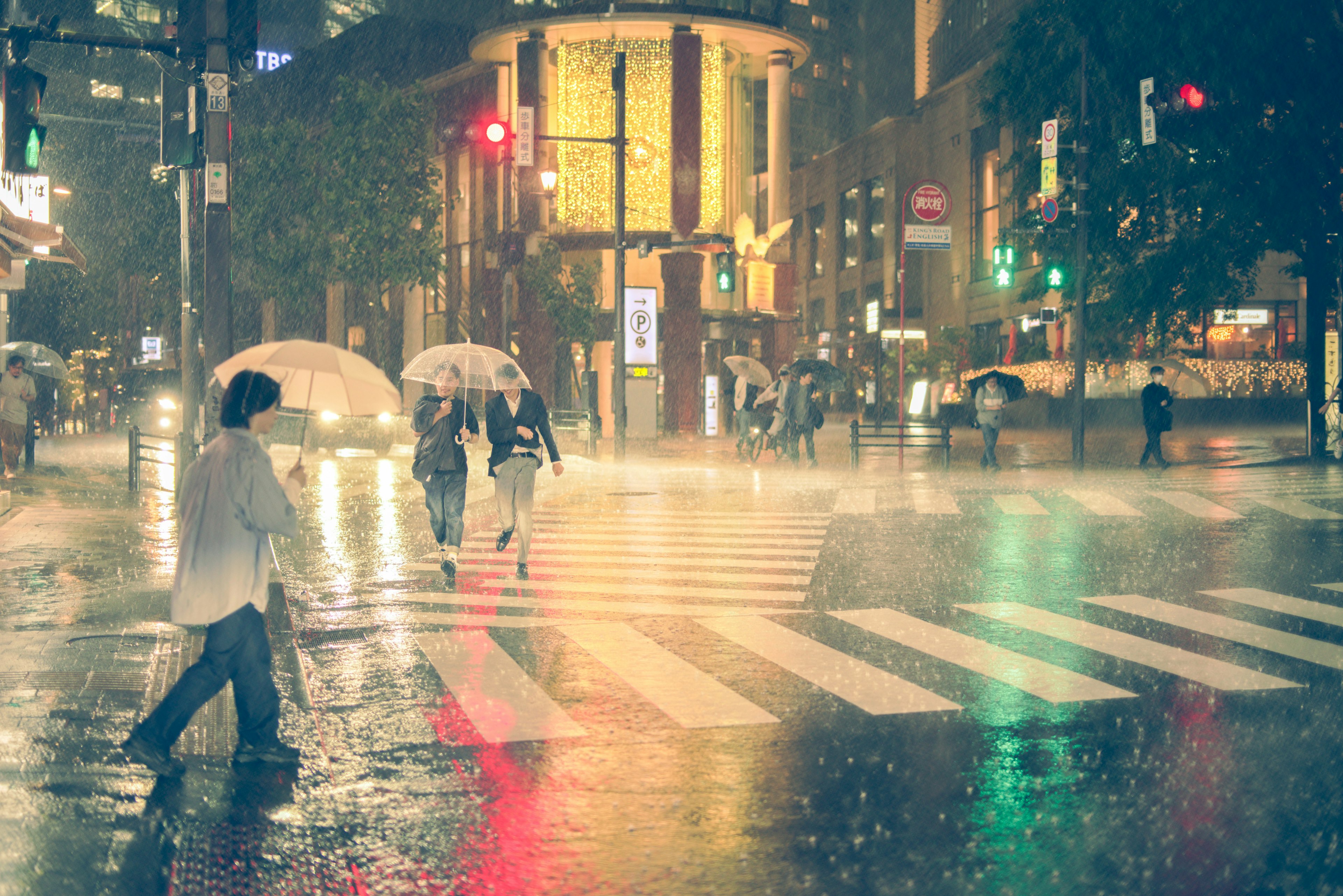 Personas caminando bajo la lluvia con paraguas en una intersección de la ciudad por la noche