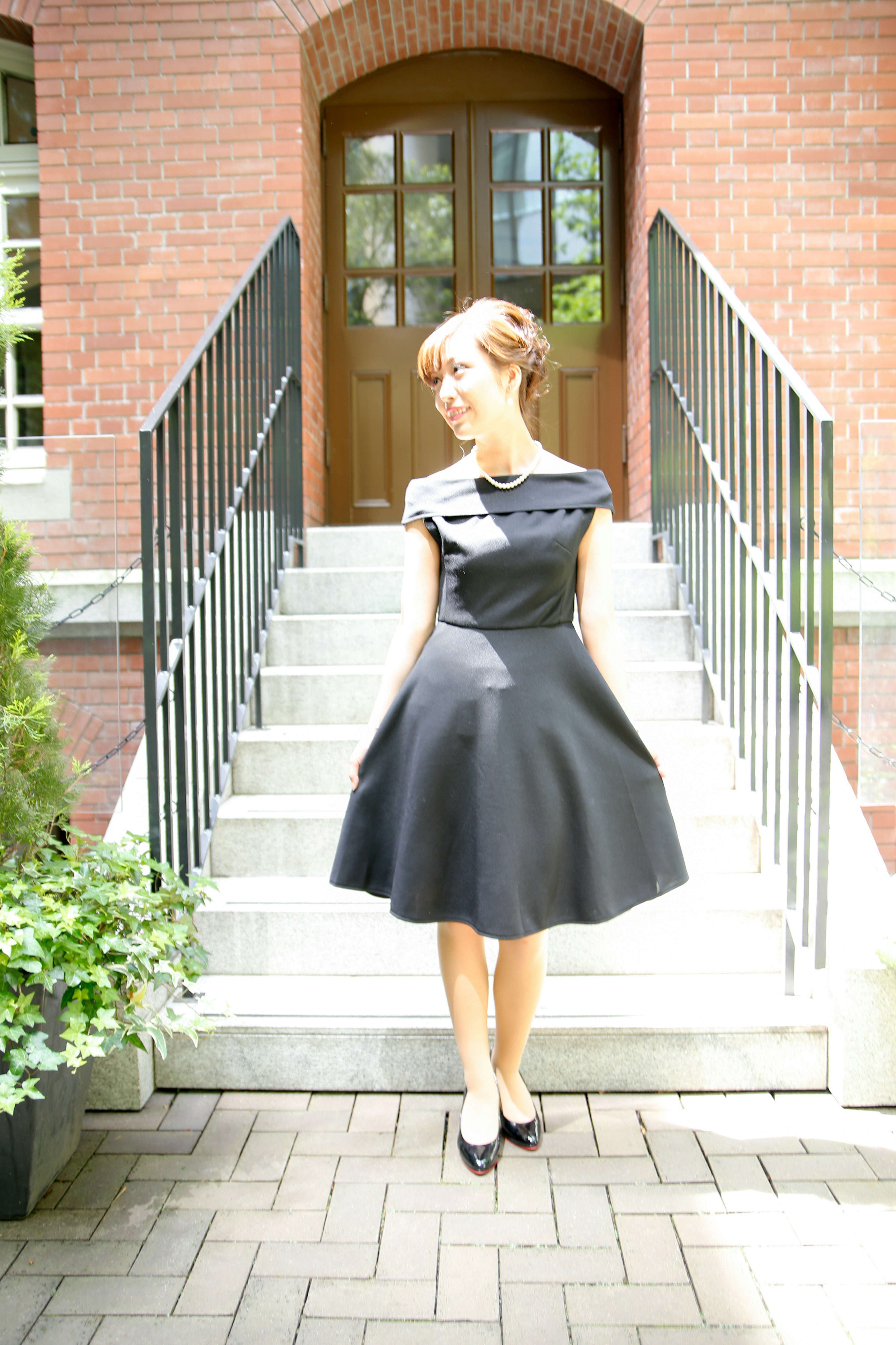 A woman in a black dress standing in front of stairs