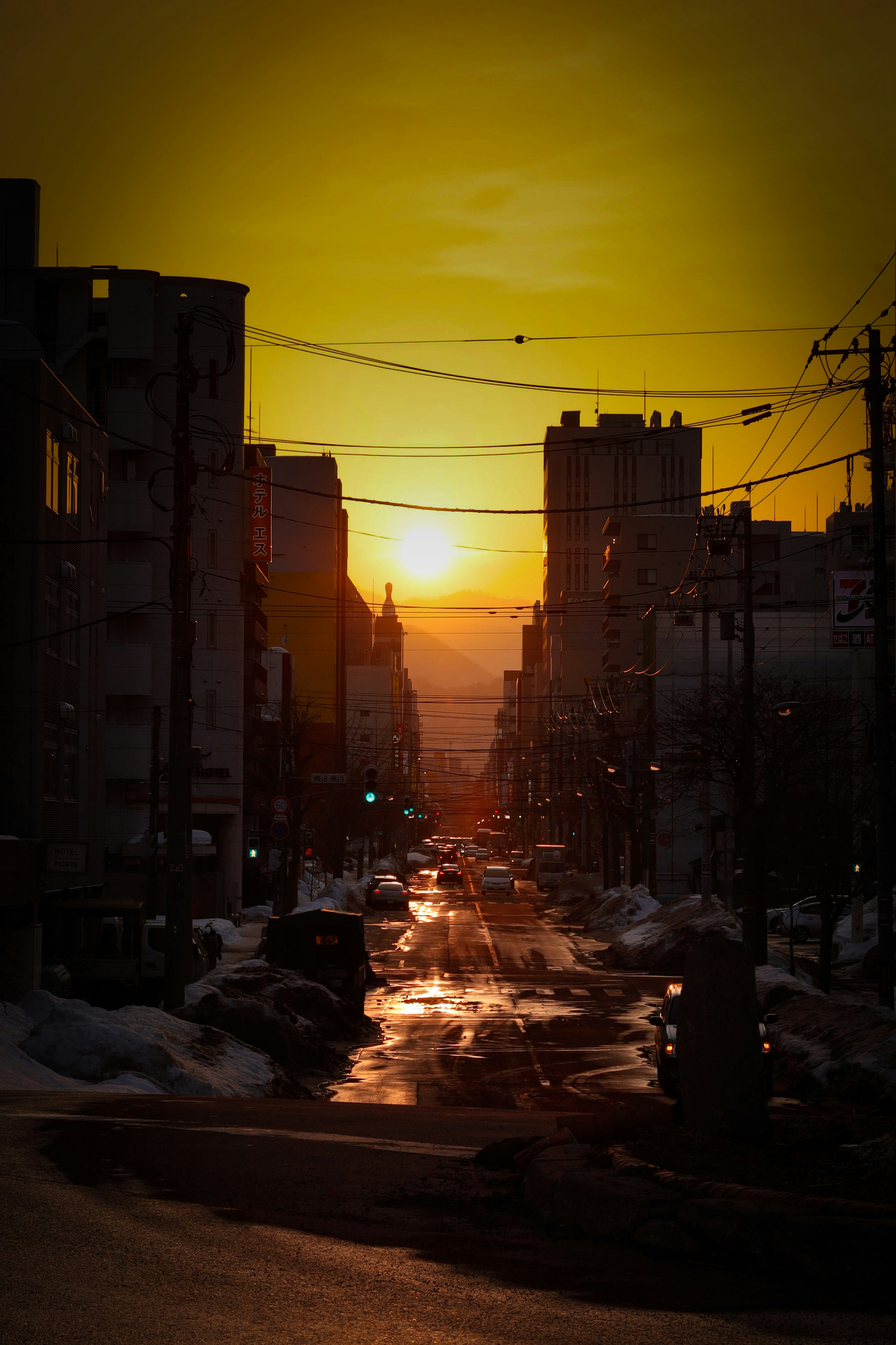 Paysage urbain au coucher du soleil avec des bâtiments en silhouette et des reflets sur la route