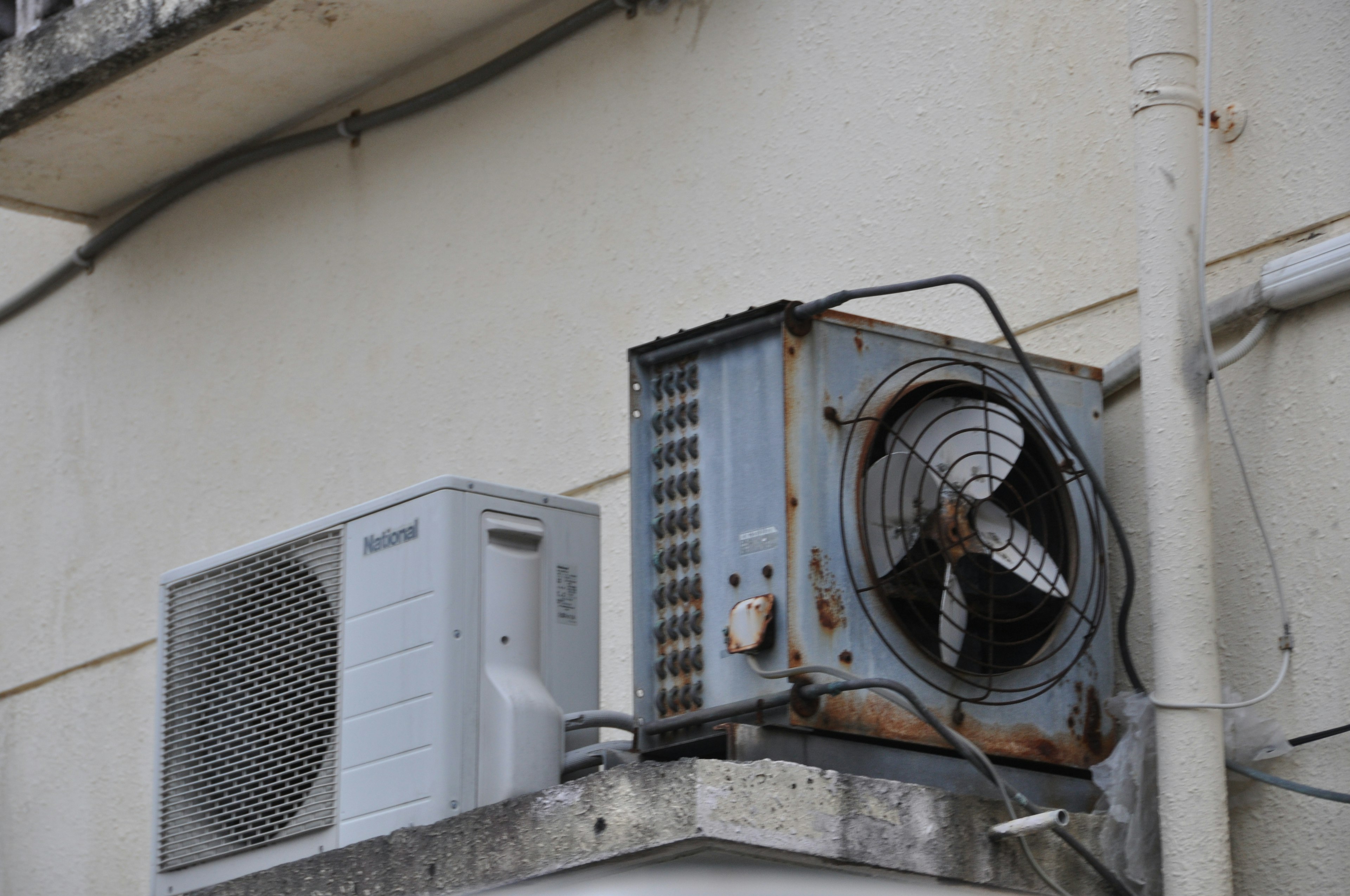 Image of an old air conditioning unit mounted on a wall featuring a rusty fan and two units