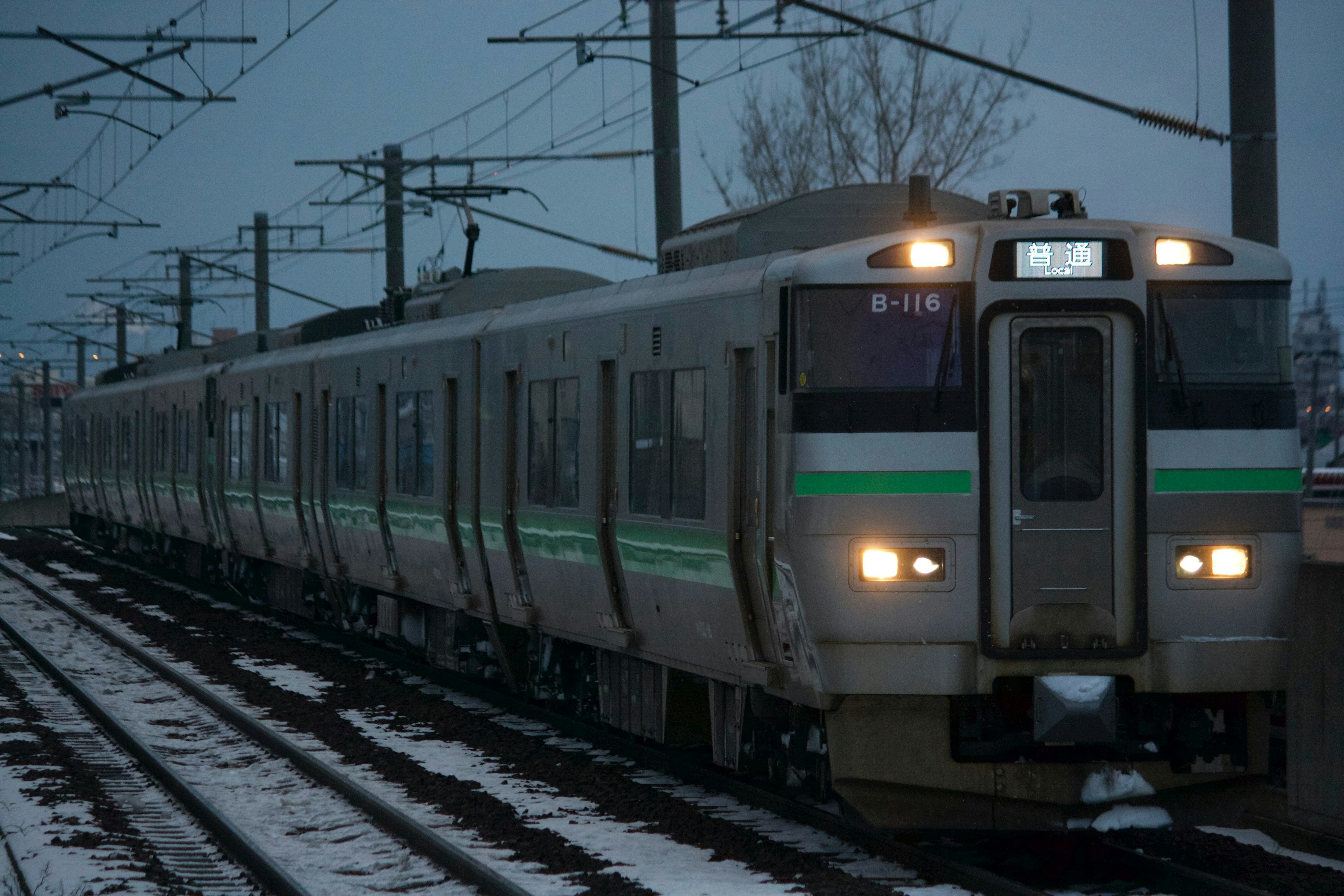 雪の中を走る緑のストライプの電車