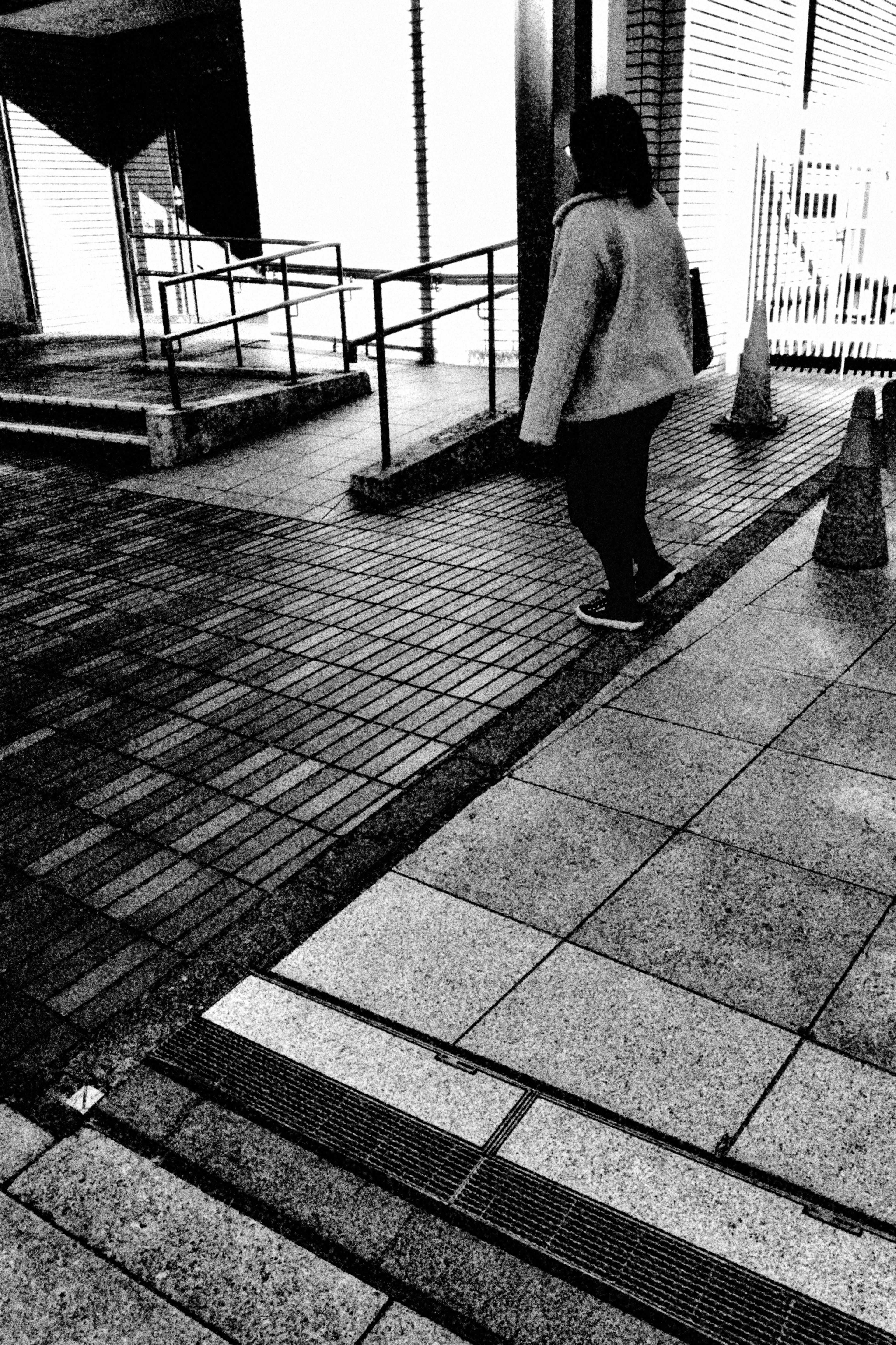 A person walking in a black and white urban setting with guardrails and paved sidewalks