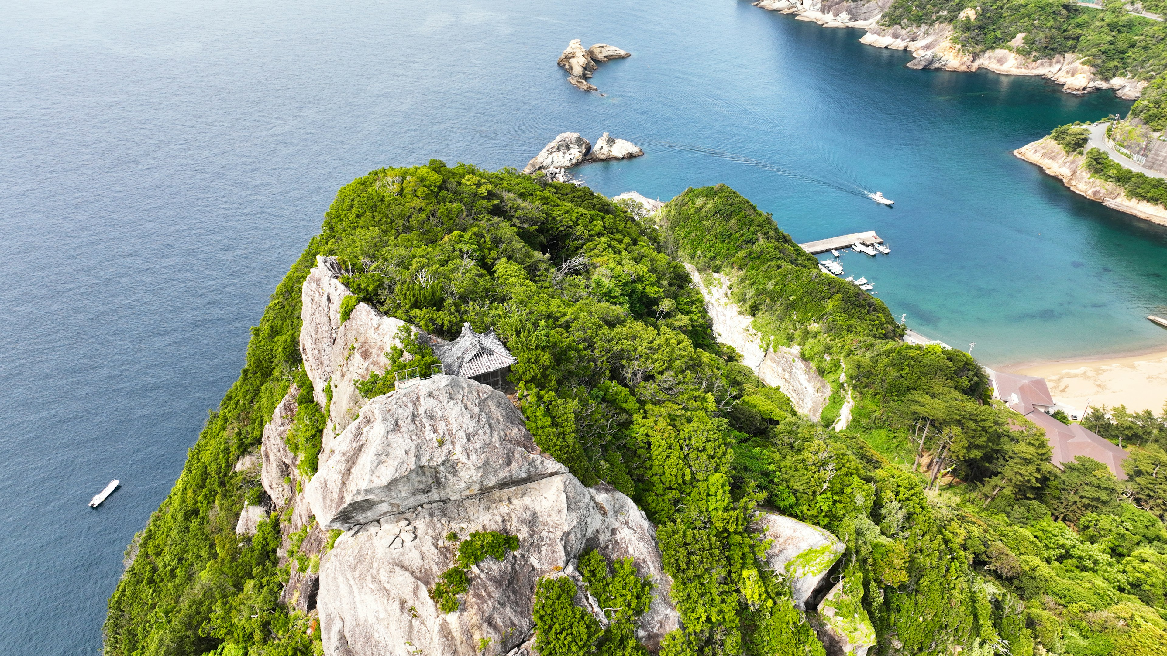 Montagne verdoyante surplombant une mer bleue avec des rochers et des bateaux visibles