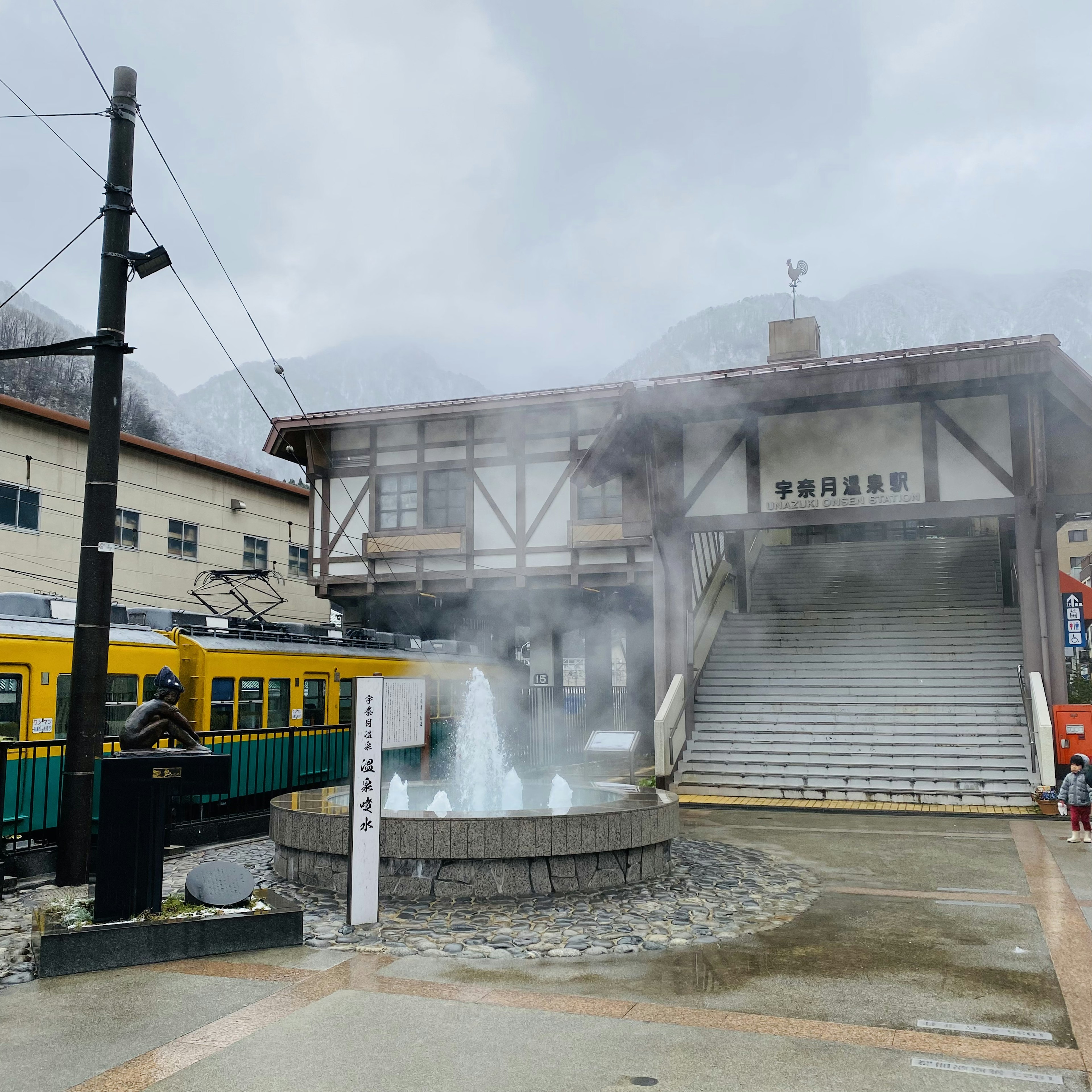 温泉街の駅舎と蒸気の立ち上る温泉の噴水