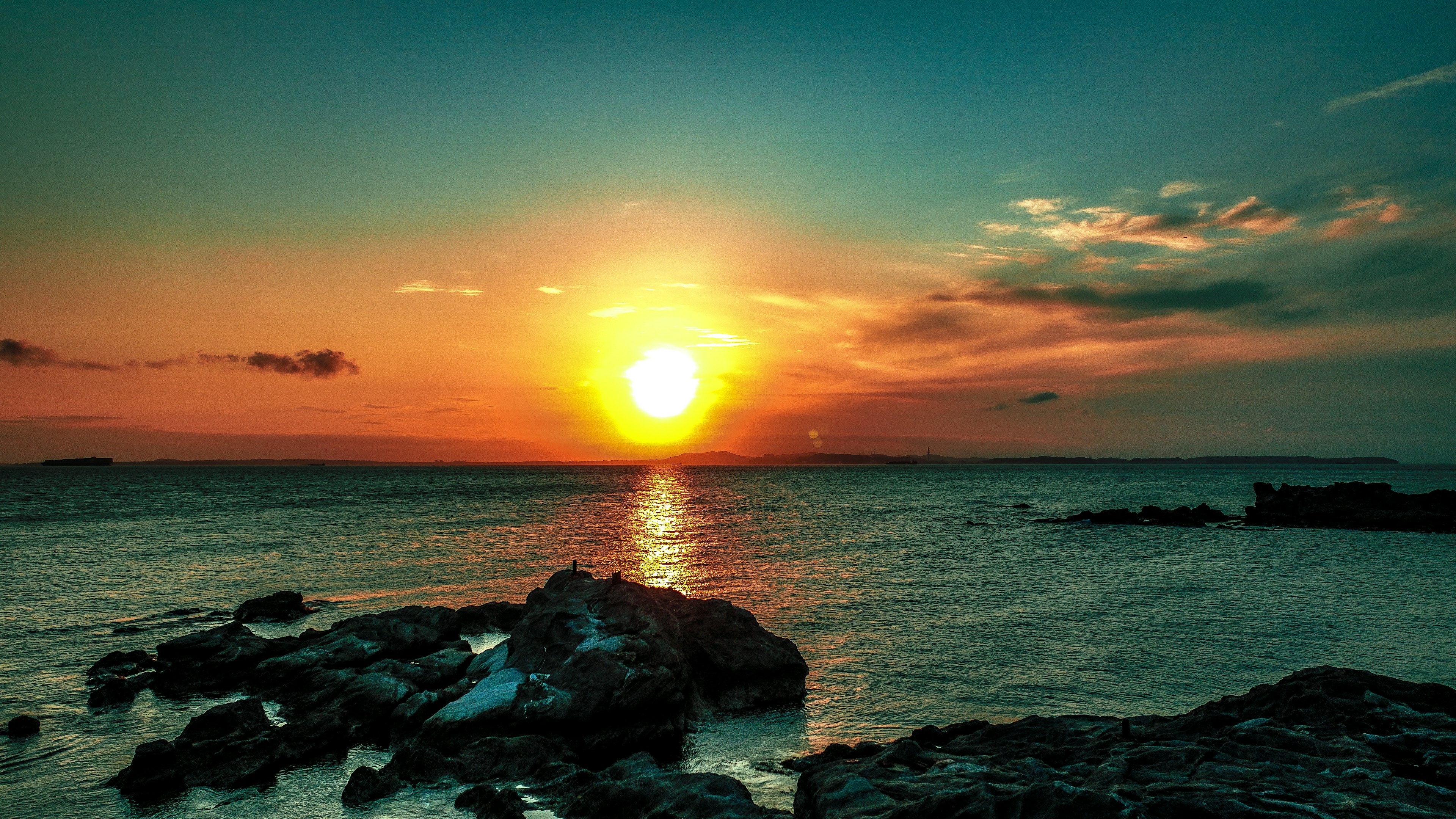 Atardecer sobre el océano con rocas y reflejos en el agua