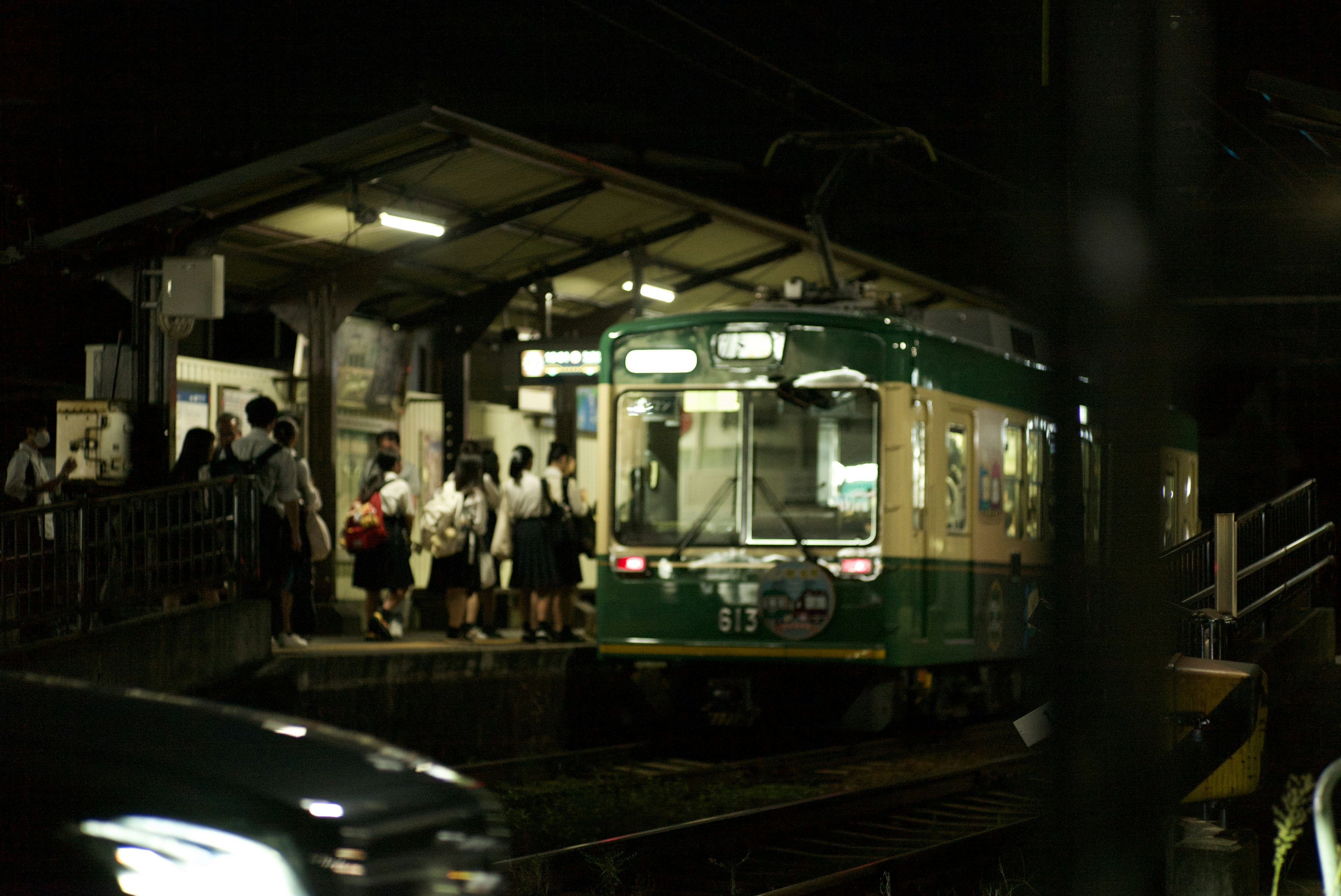 夜の駅で停車中の緑色の電車と乗客