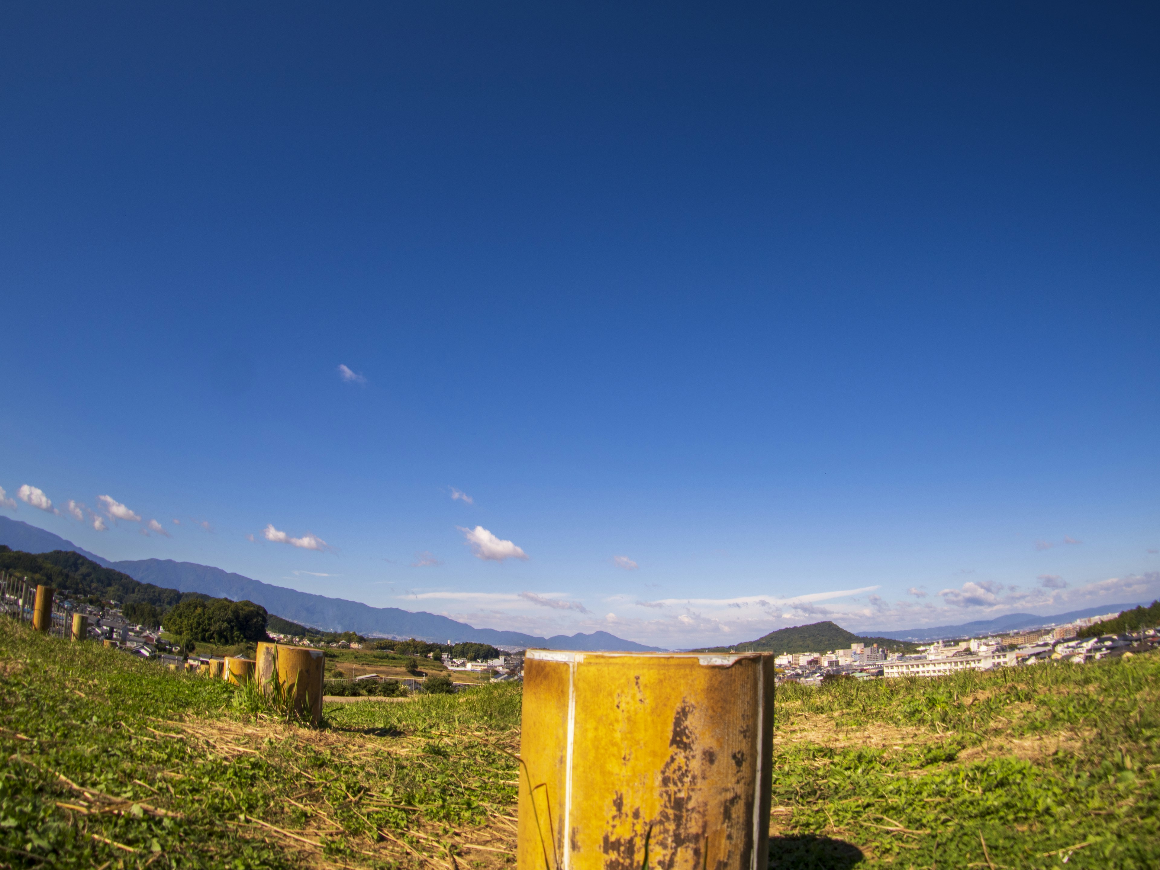 Yellow cylindrical object in a grassy field under a blue sky