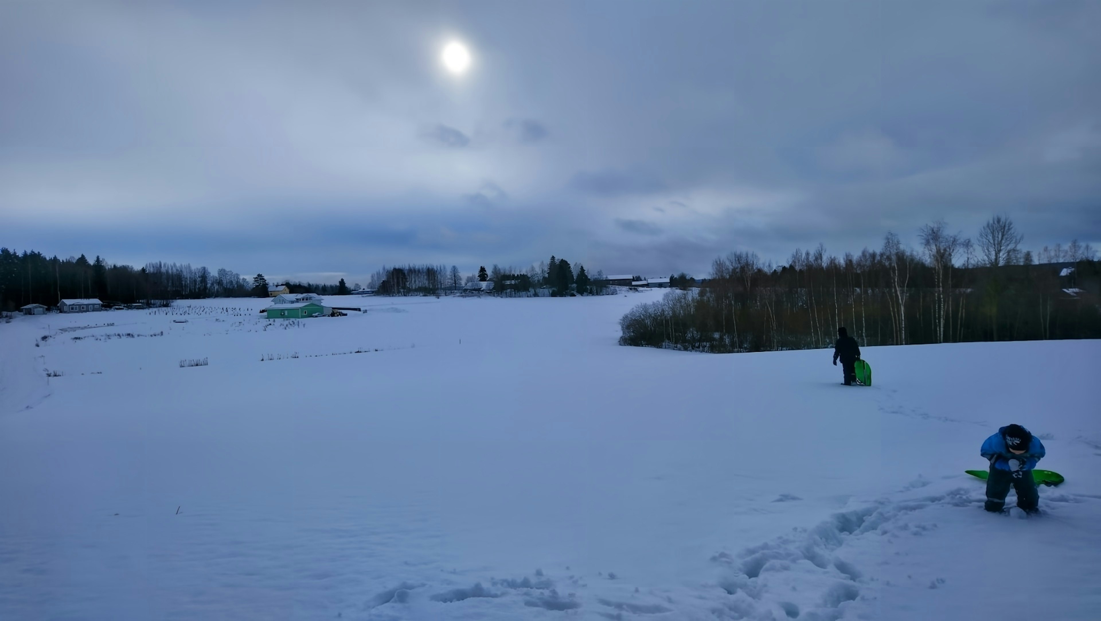 Ampio paesaggio innevato con un sole brillante nel cielo blu e un bambino che trascina una slitta