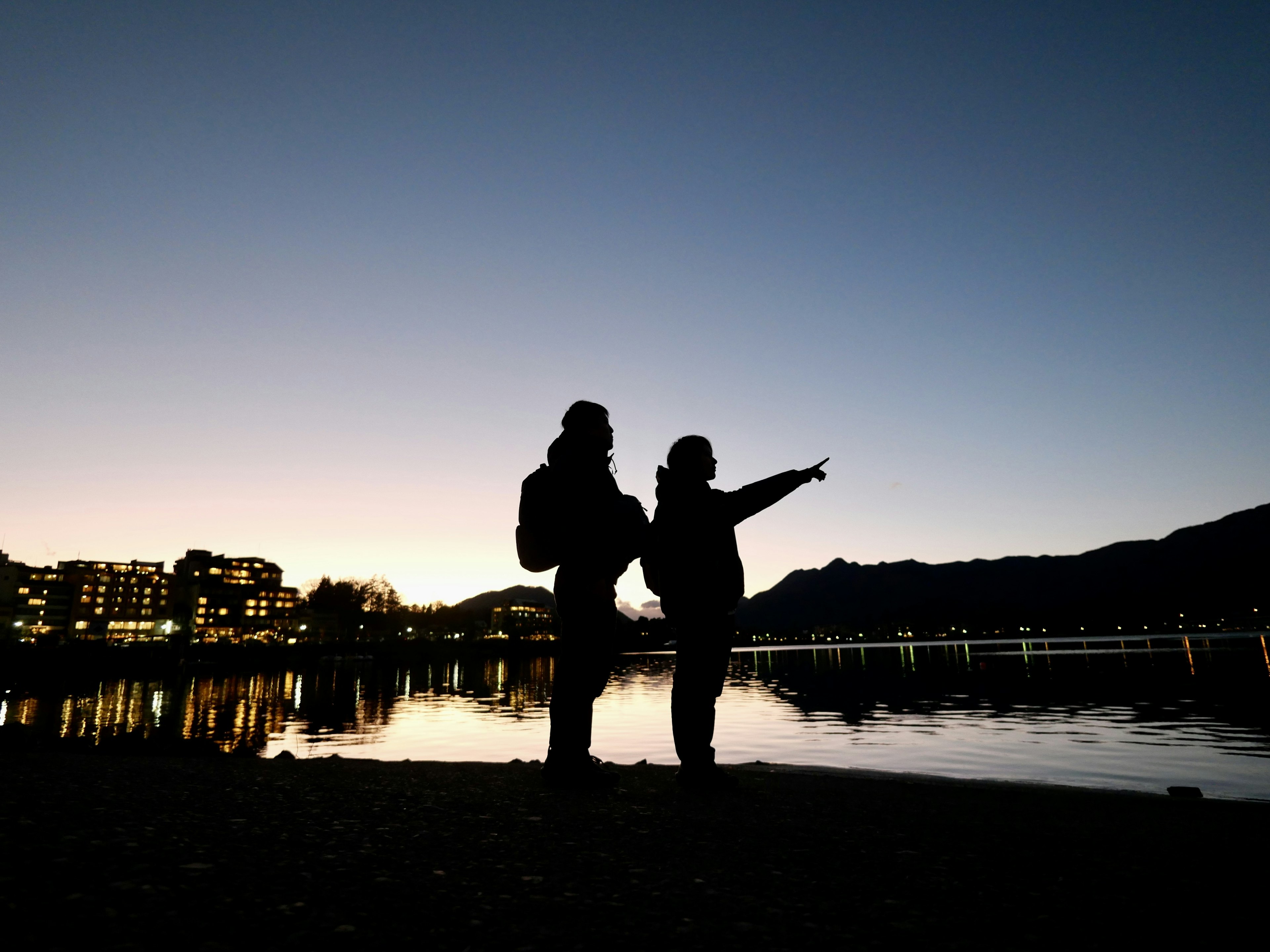 Siluetas de dos personas de pie junto al lago al anochecer