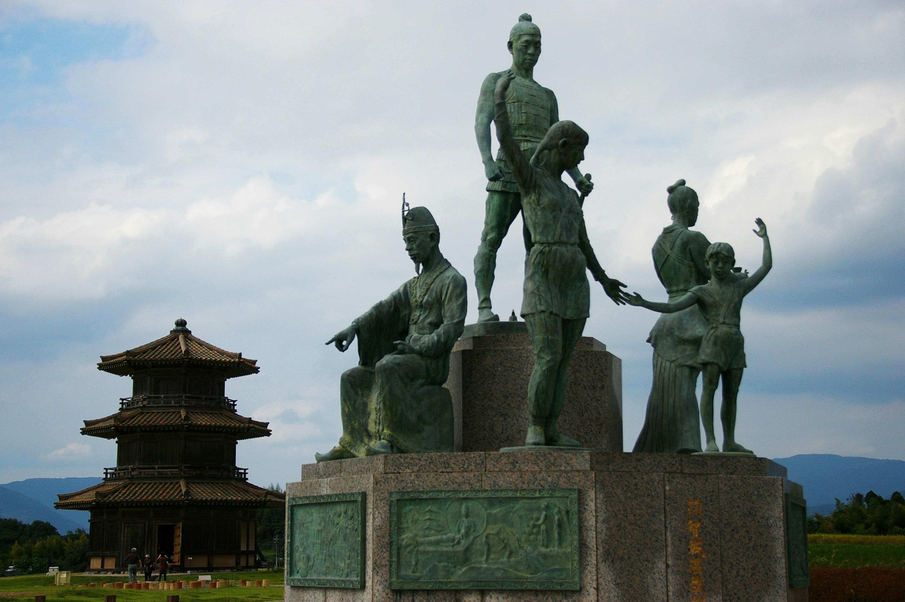 Bronze sculptures of figures in a park with an ancient building in the background