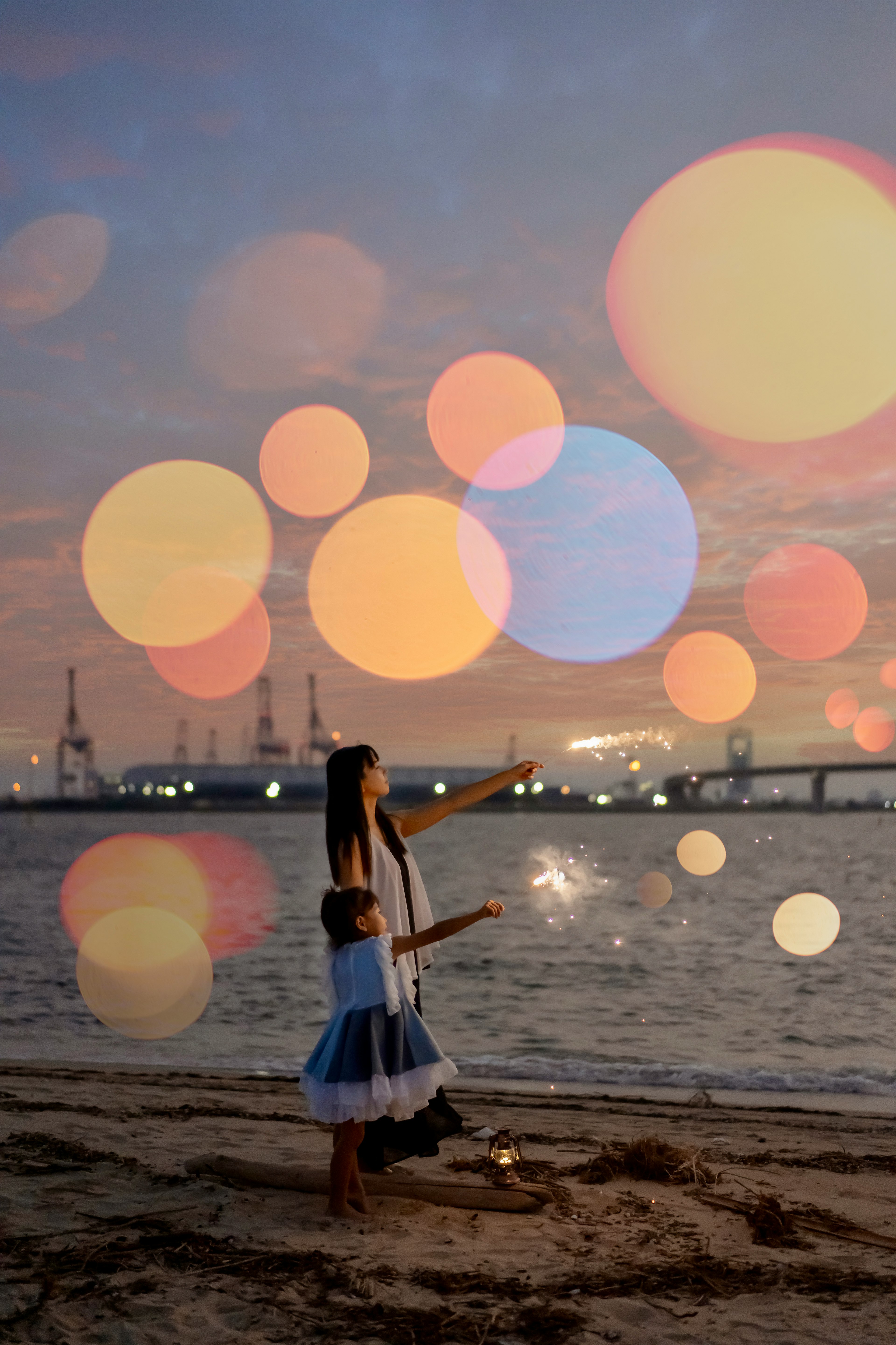 夕日を背景に砂浜で花火を楽しむ親子のシルエットがある