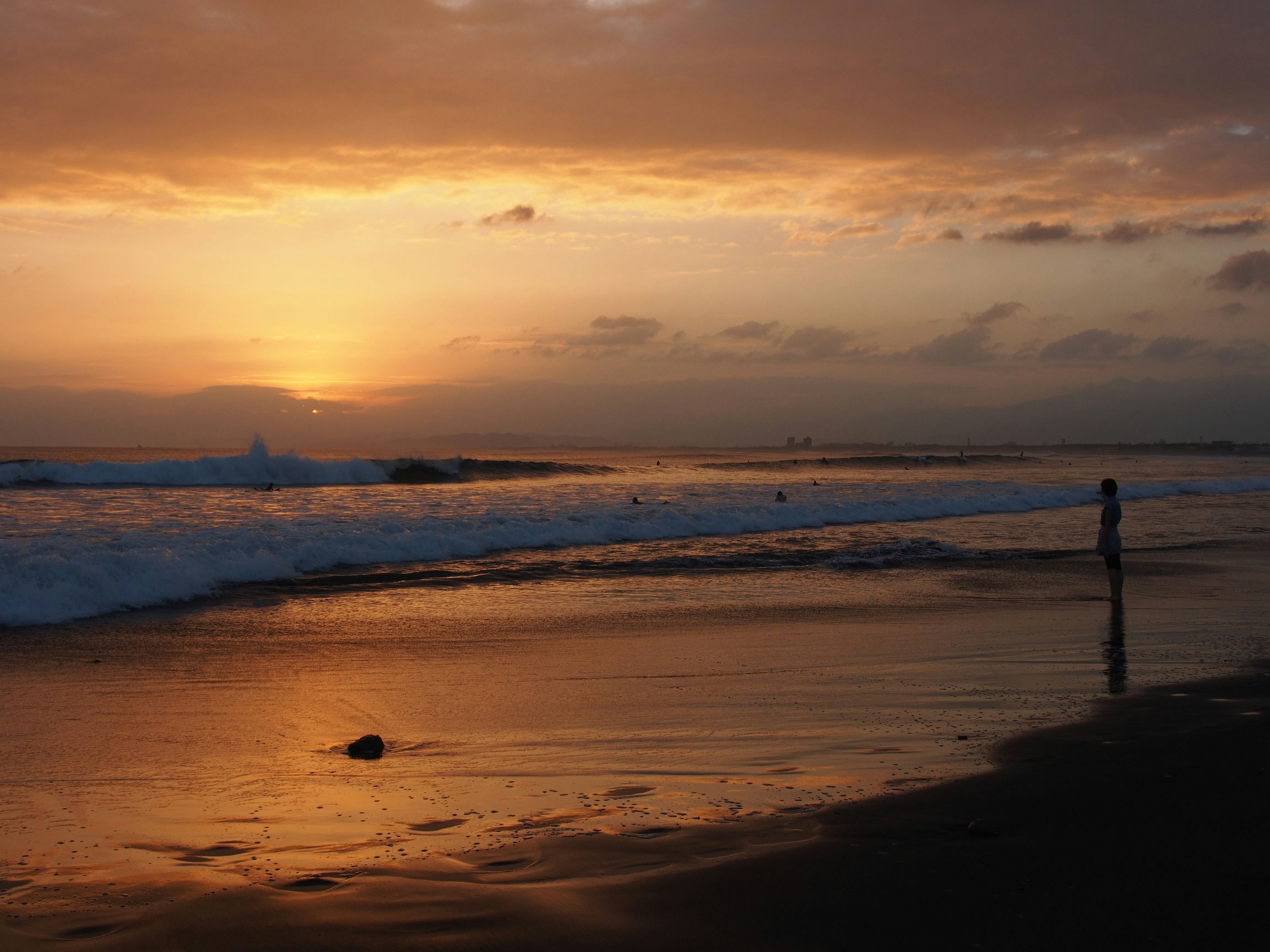 Seseorang berdiri di tepi pantai saat matahari terbenam Warna oranye yang indah di langit