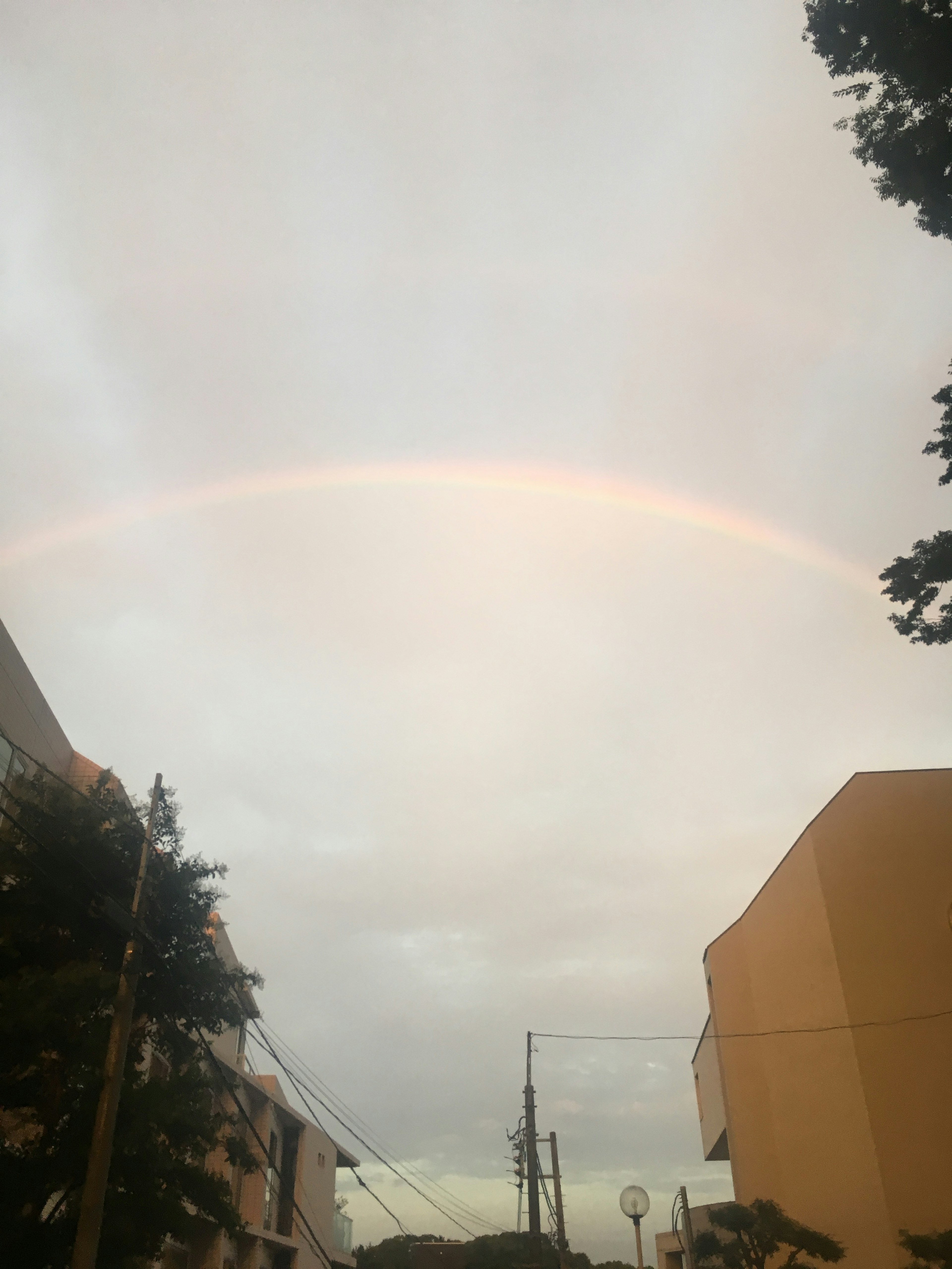 Faint rainbow arching across a cloudy sky with buildings