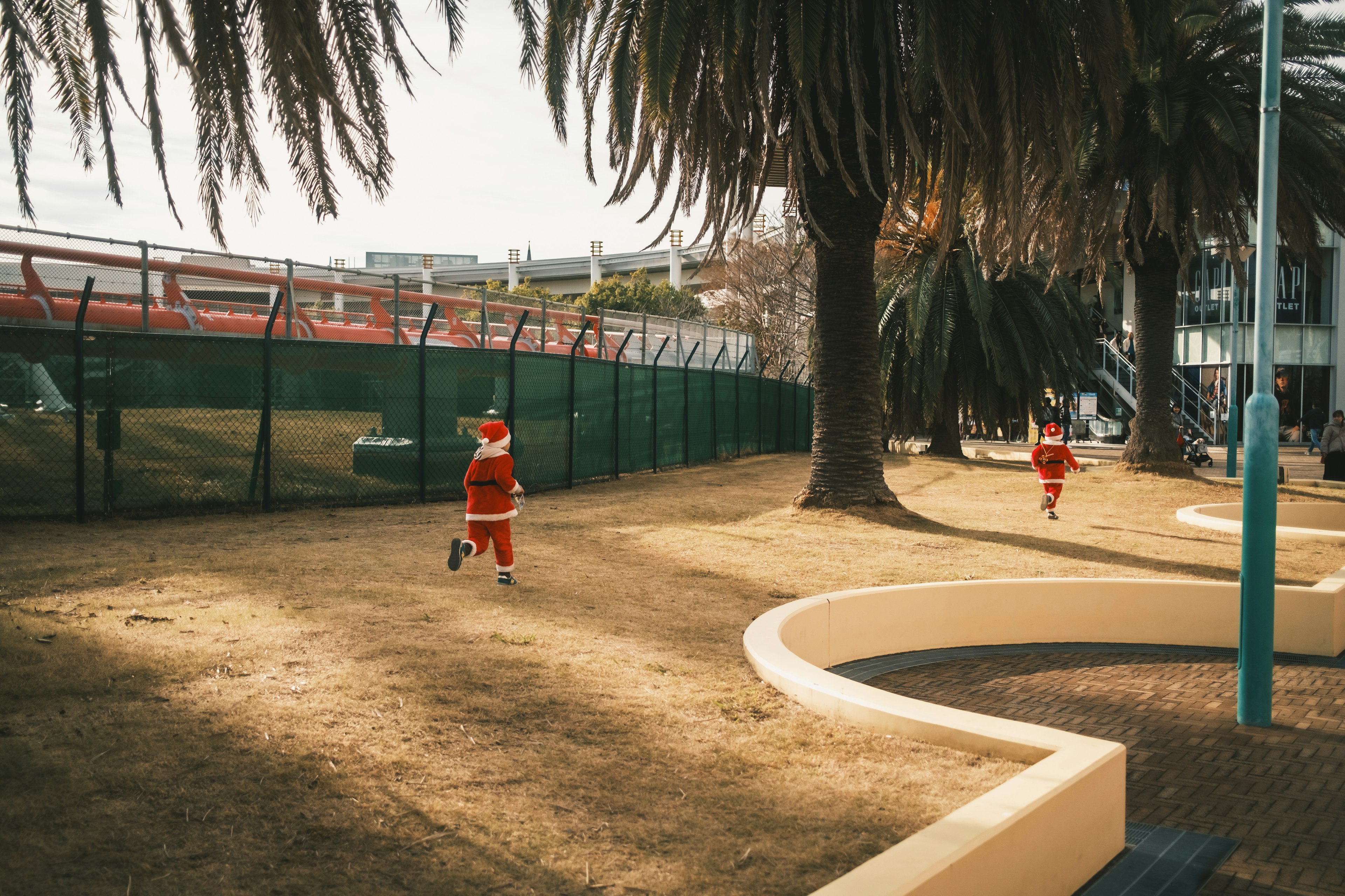 Due bambini vestiti da Babbo Natale che corrono in un parco