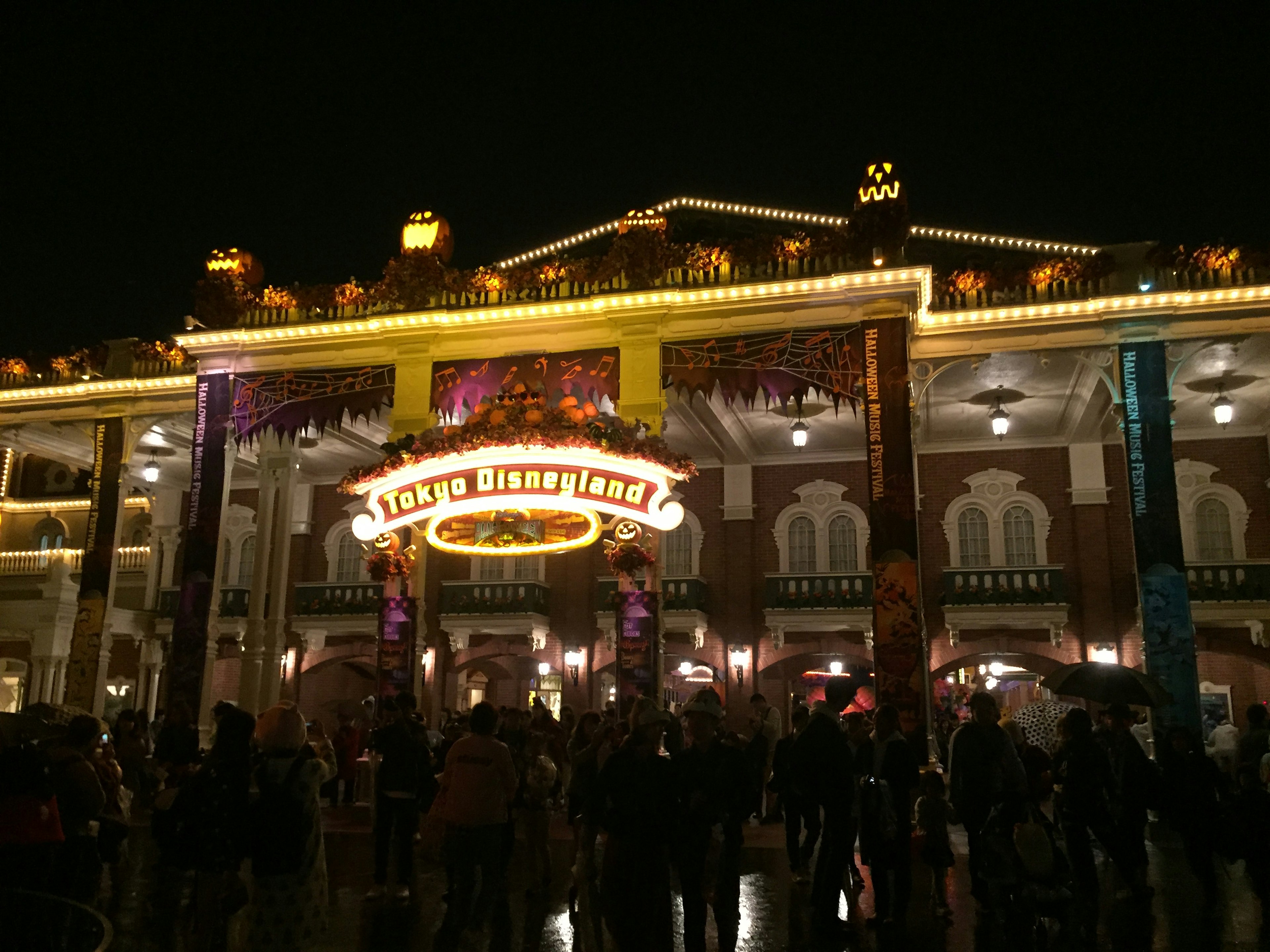 Crowd gathered in front of a brightly lit building with colorful decorations at night in a theme park