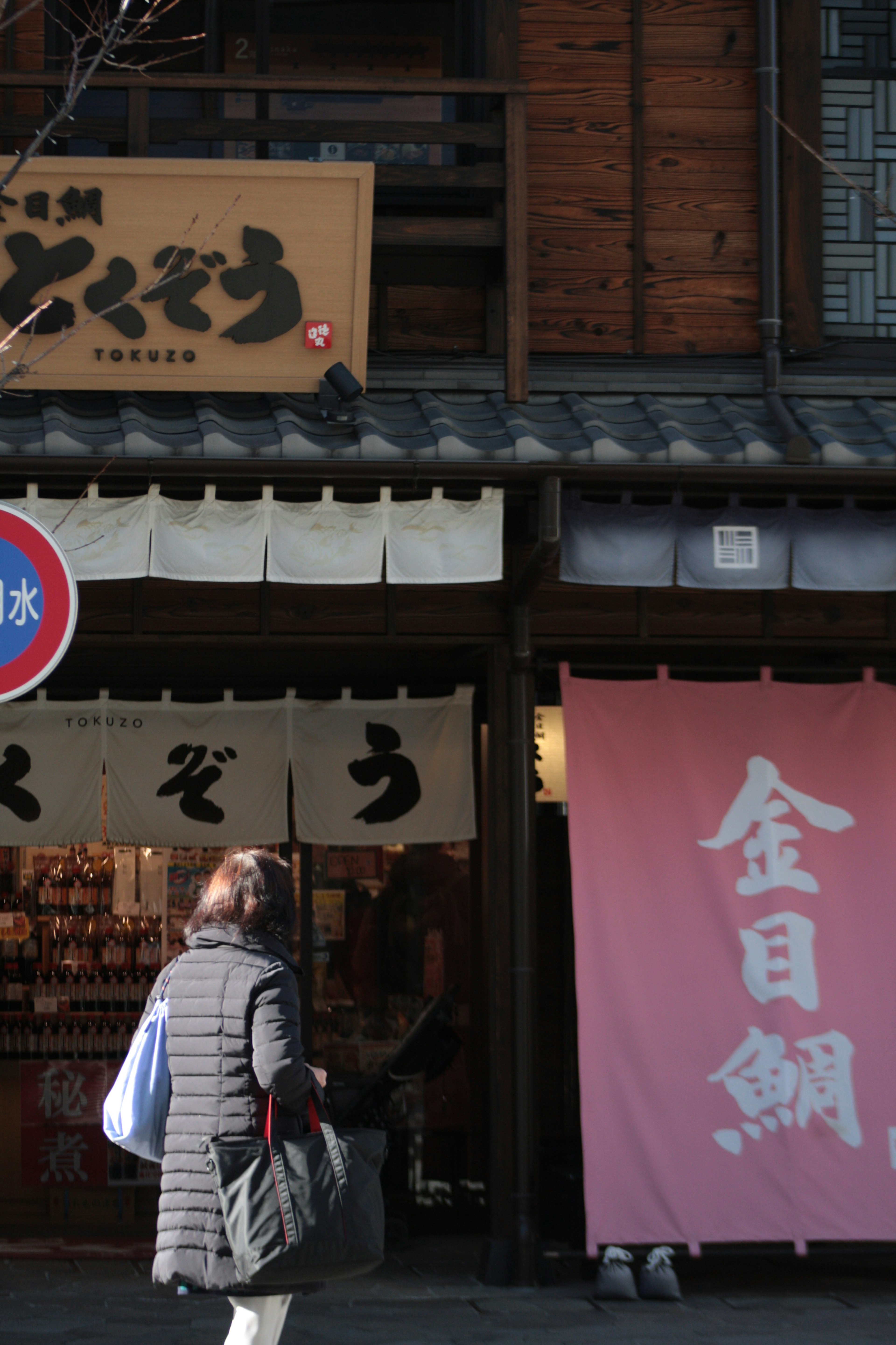 木製の建物の前にある店舗の看板とピンクの布幕