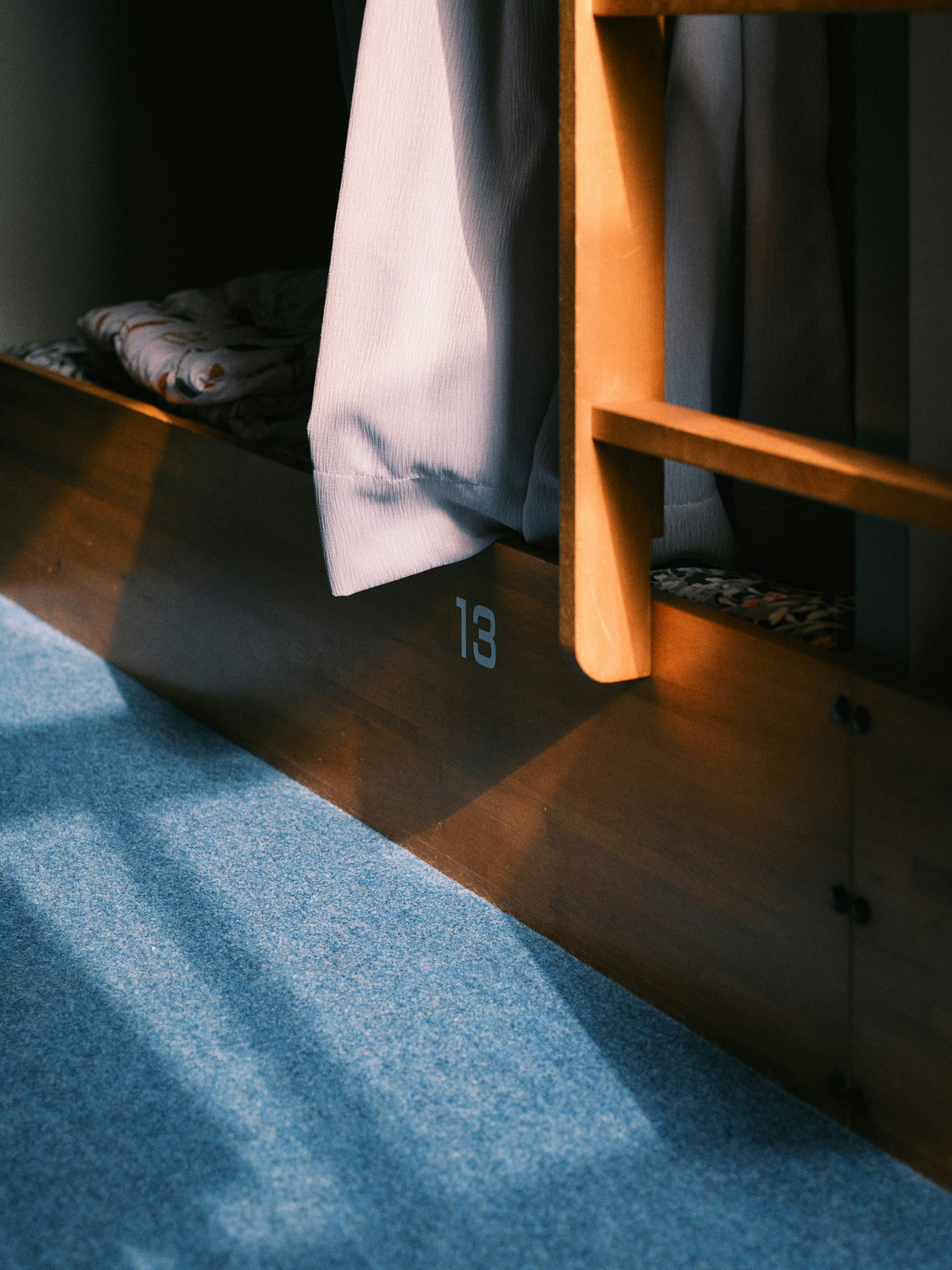 Wooden bed frame with number 13 visible and curtain casting shadows