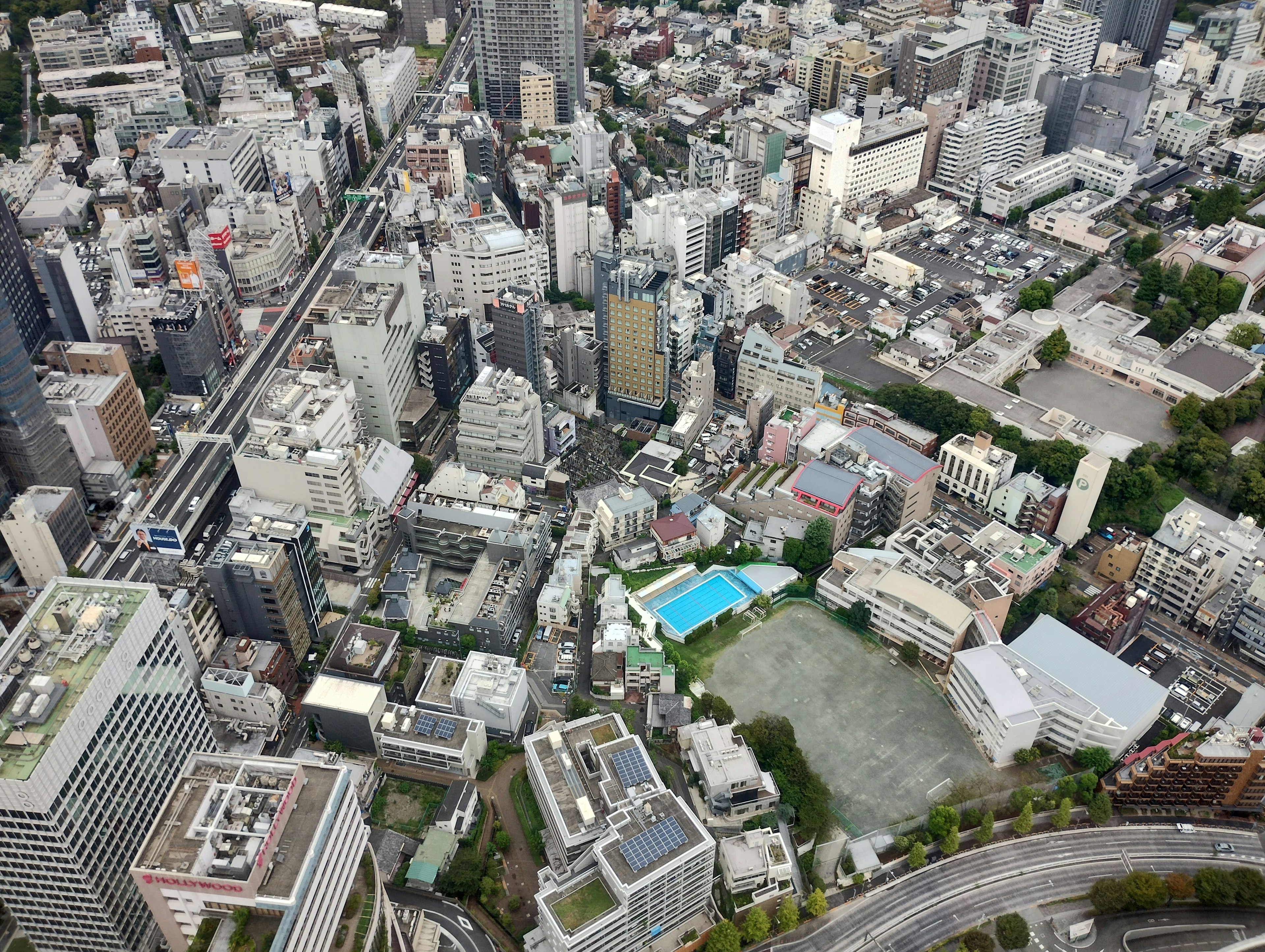 Aerial view of a cityscape with tall buildings featuring a park and swimming pool