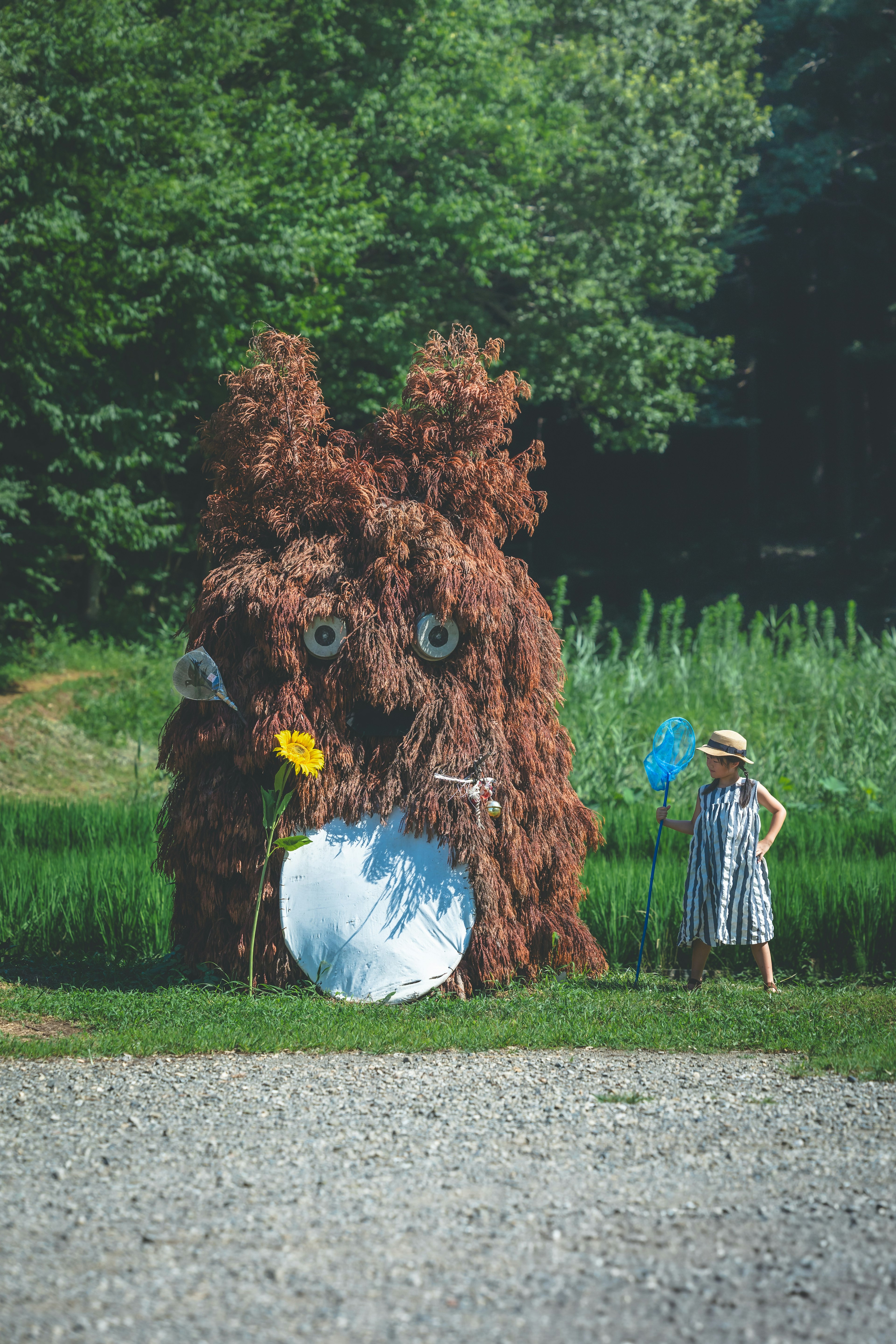 Un gran personaje marrón parecido a un árbol frente a un fondo verde con una niña sosteniendo flores