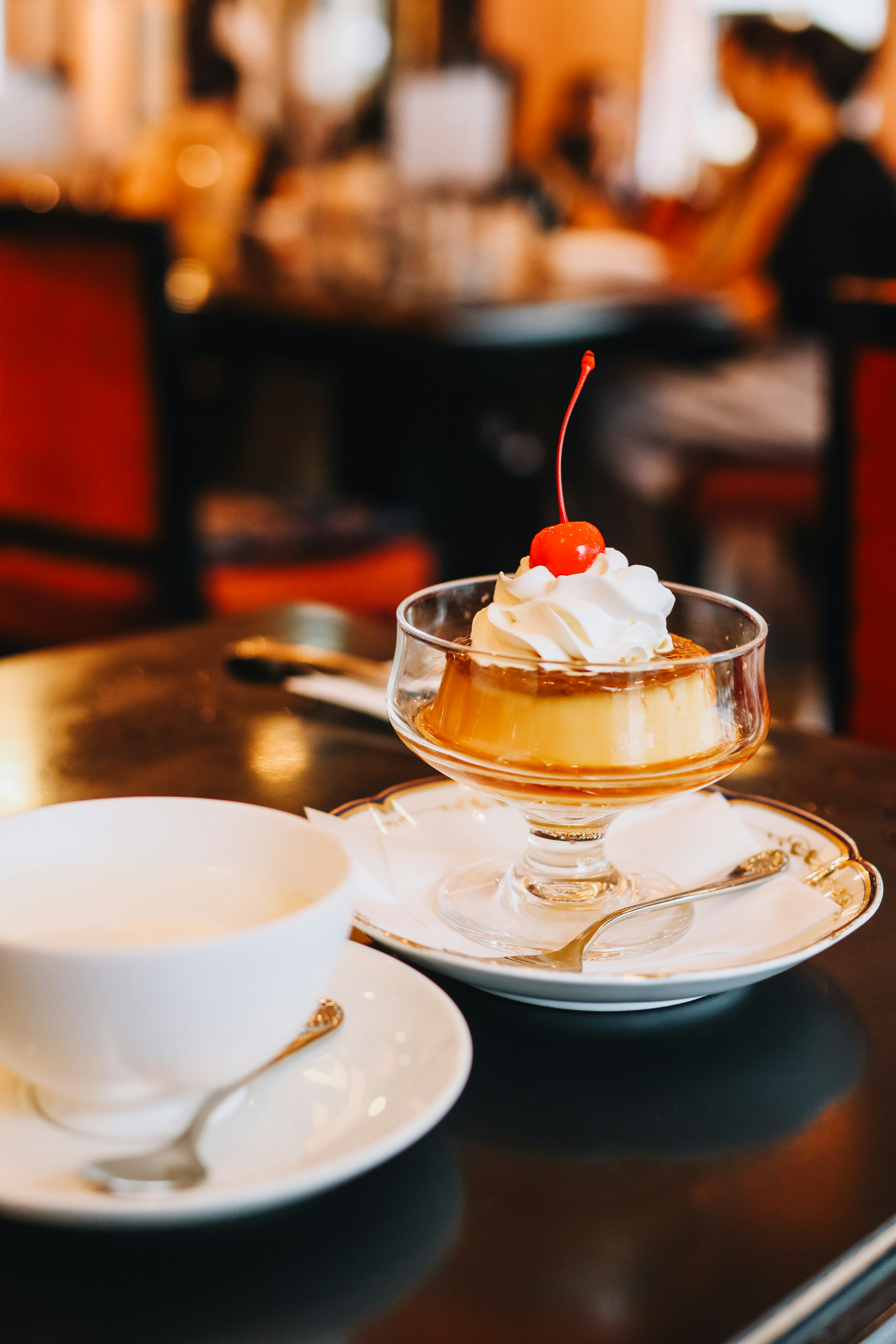 Dessert avec de la crème fouettée et une cerise sur le dessus servi dans un plat en verre à côté d'une tasse blanche