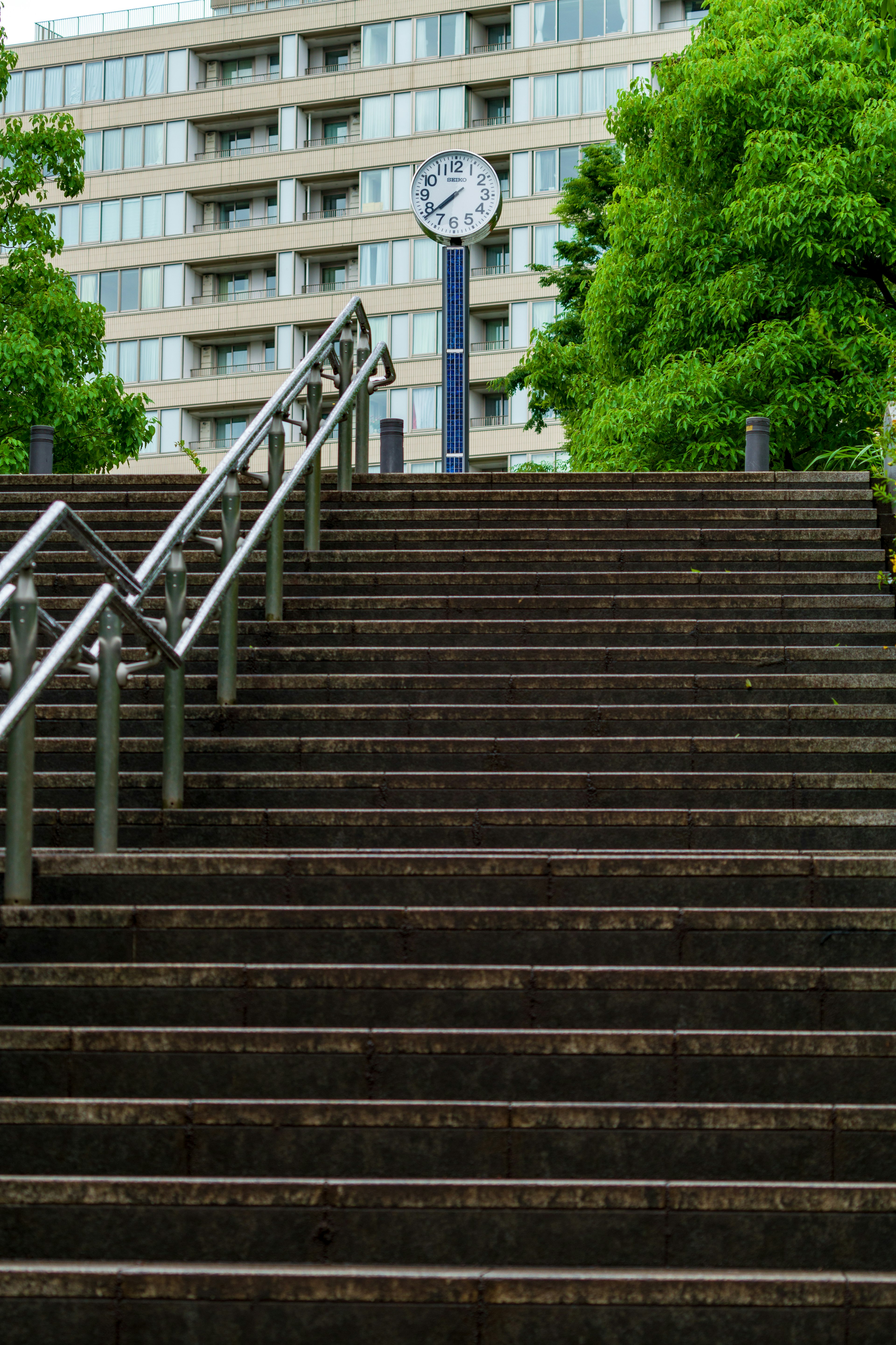 階段の上にある時計と緑の木々を背景にした都市の風景